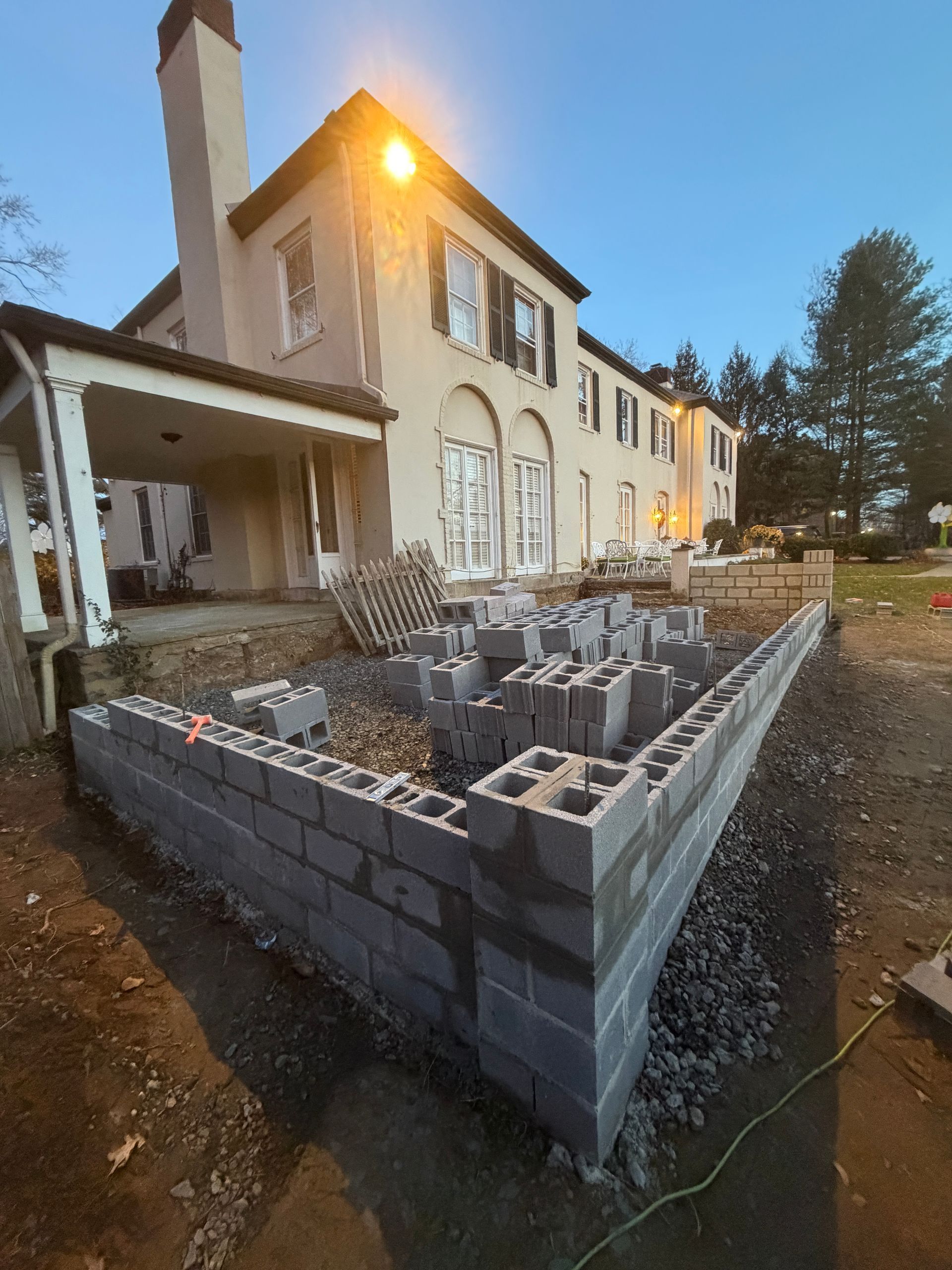 Construction of a retaining wall with cinder blocks in front of a large house.