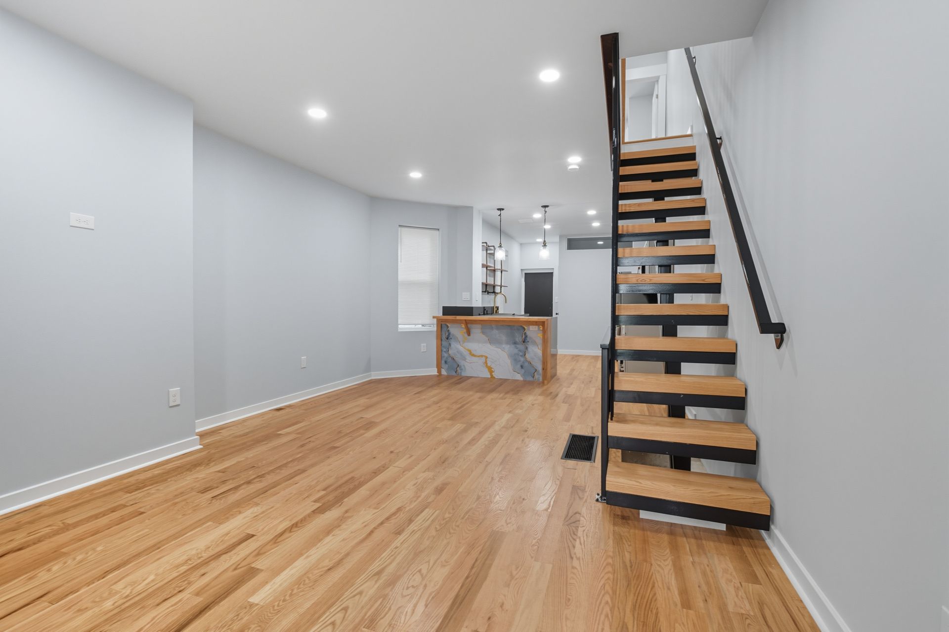 Empty, modern townhouse interior with wood floors, floating stairs, and light blue walls.