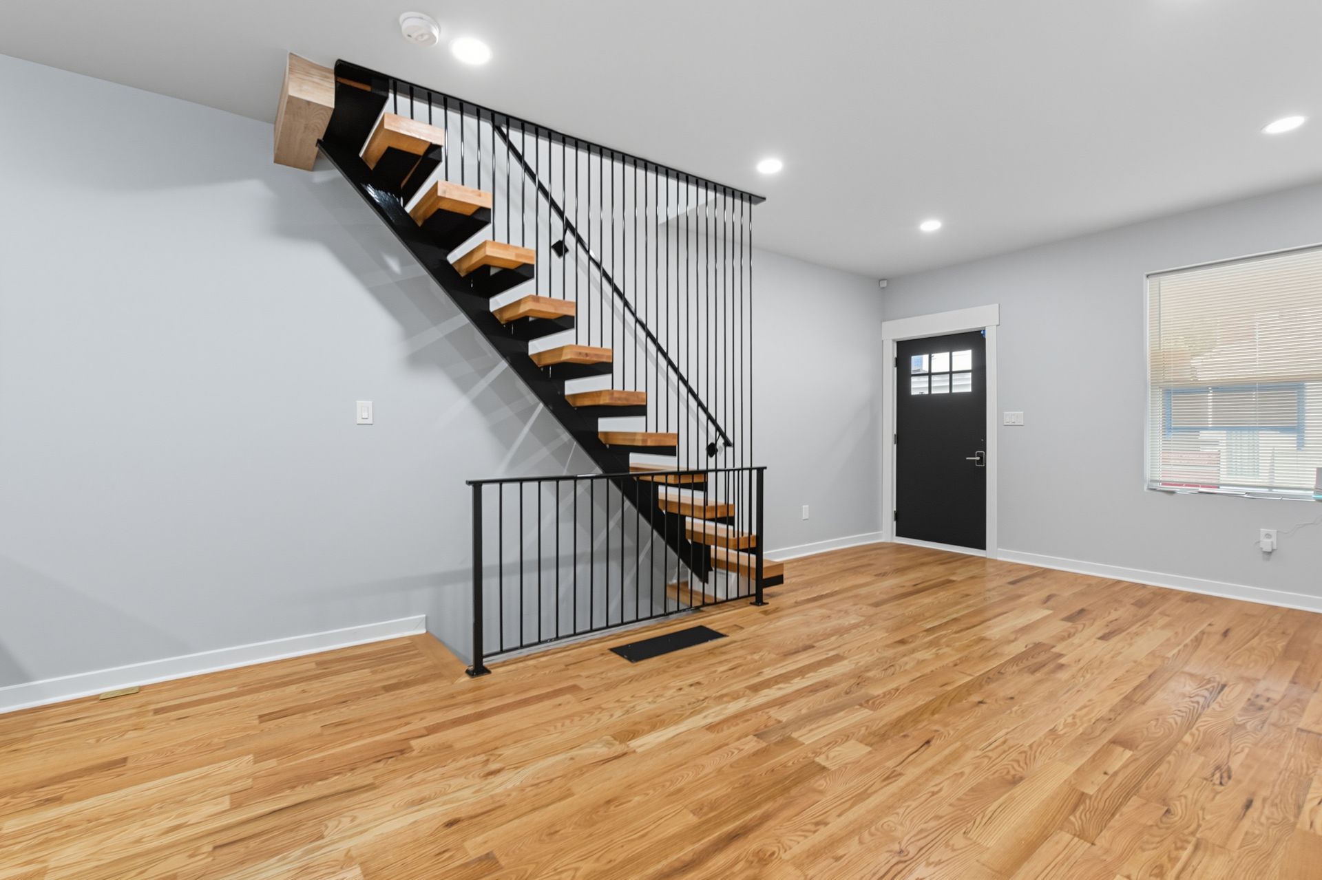 Wooden staircase with black metal railing in a room with hardwood floors, a door, and a window.