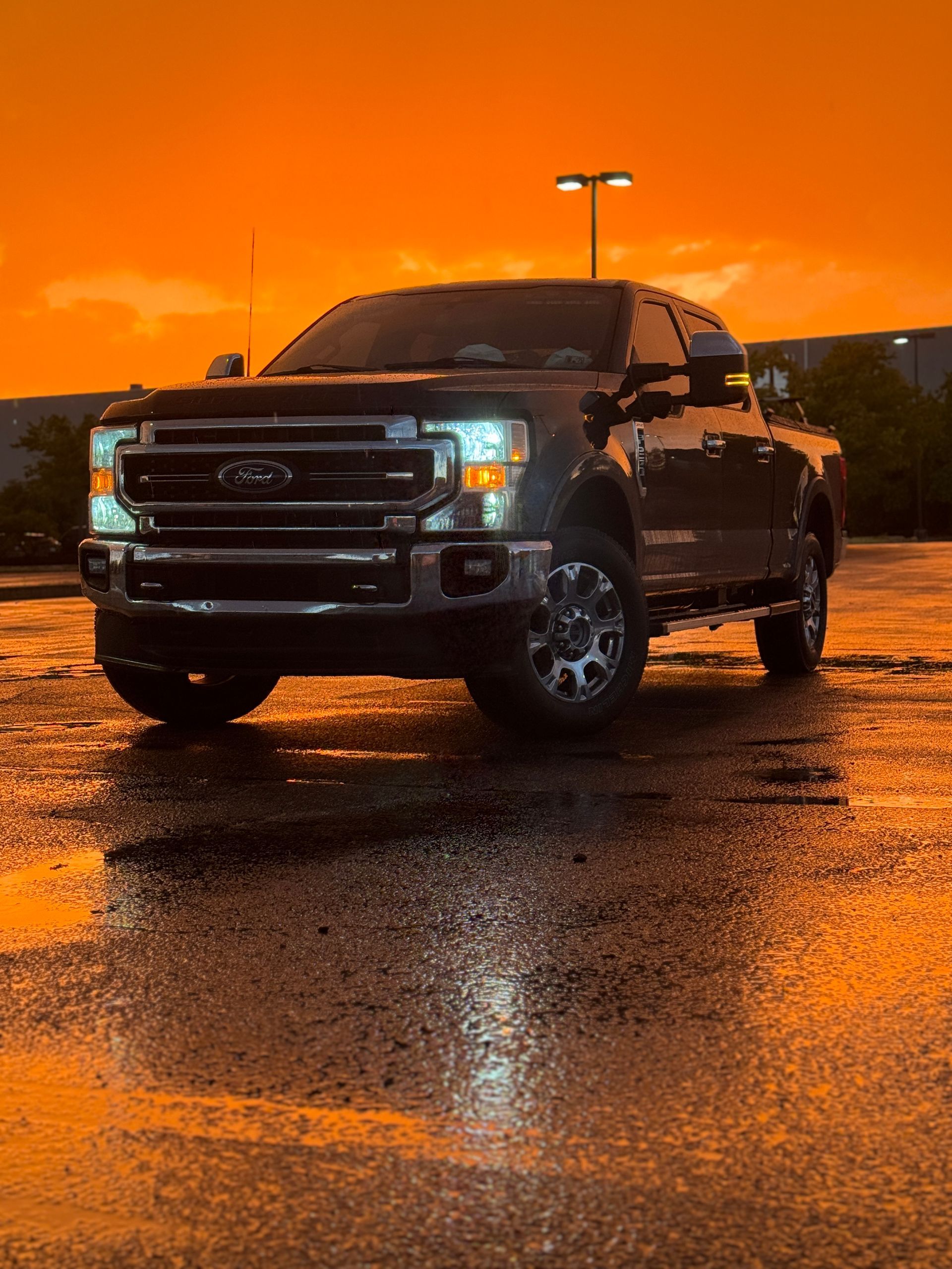 Dark Ford pickup truck parked on wet pavement, with an orange sky in the background.