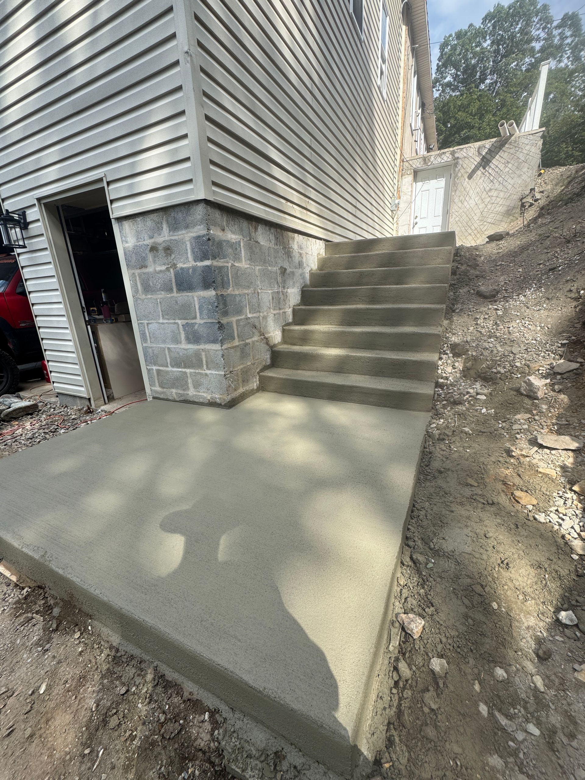 Newly poured concrete patio and stairs leading up to a building, with gravel and soil surrounding.