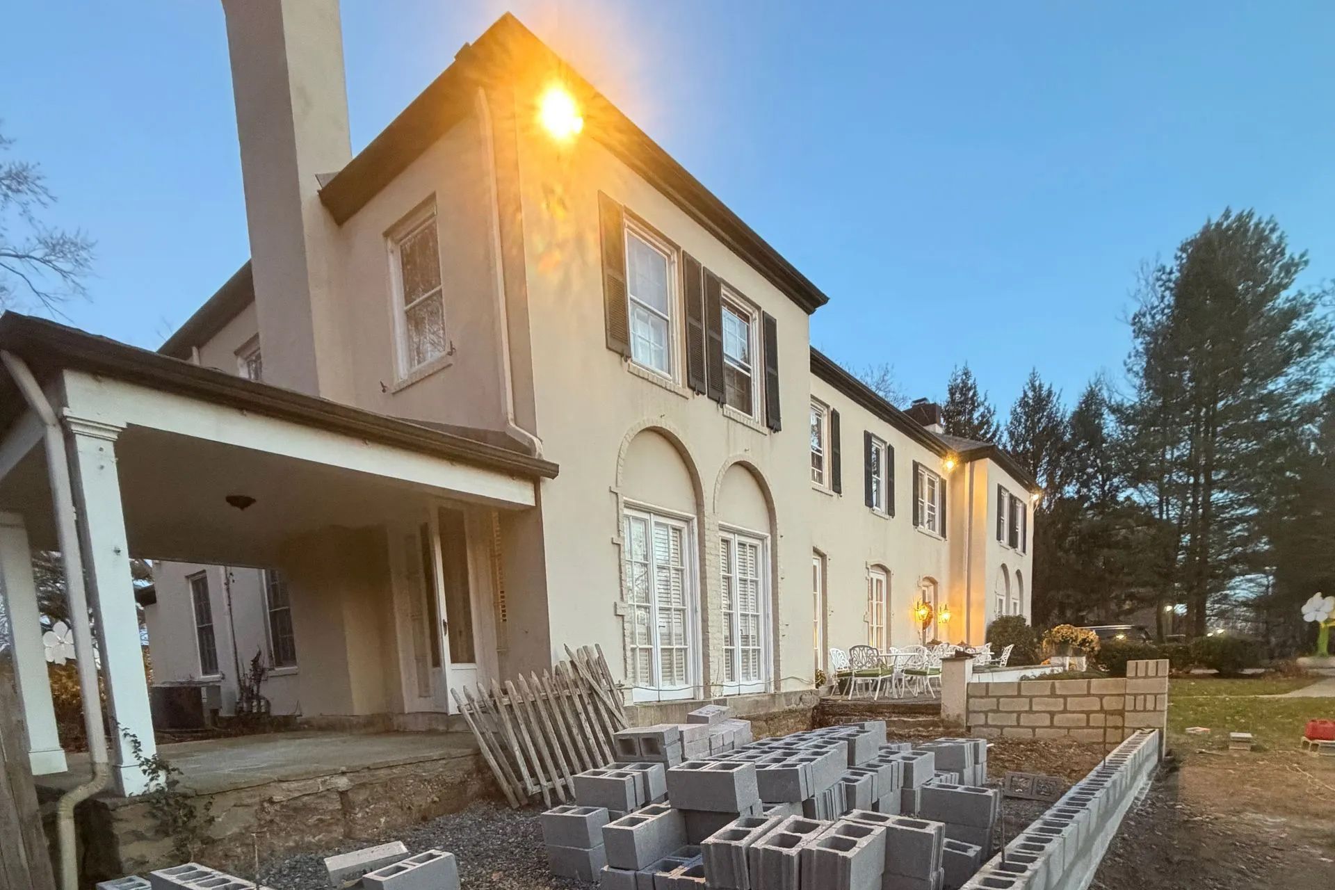 Large beige house under construction; cinder blocks in foreground. Chimney, covered porch.