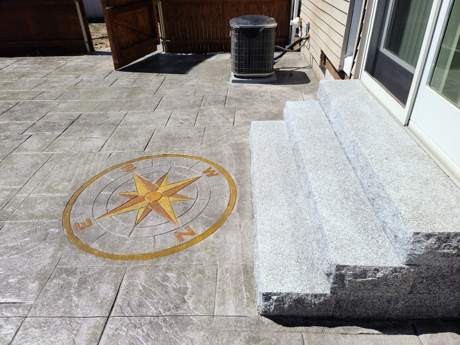 A compass rose inlay set into a gray stamped concrete patio next to light gray stone steps leading to a glass door.