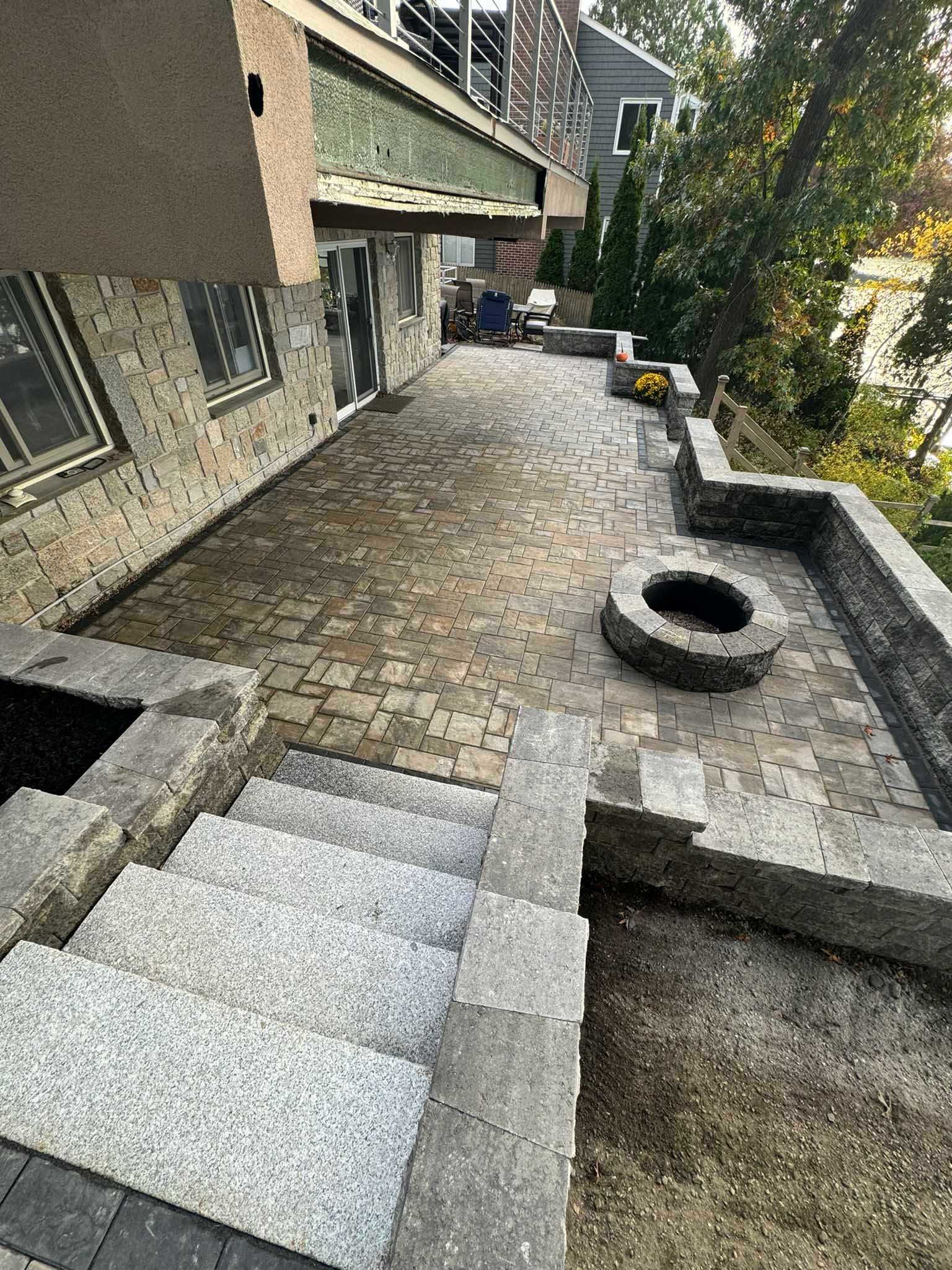 A stone patio with a built-in fire pit and gray stone steps leading up to a house under renovation.
