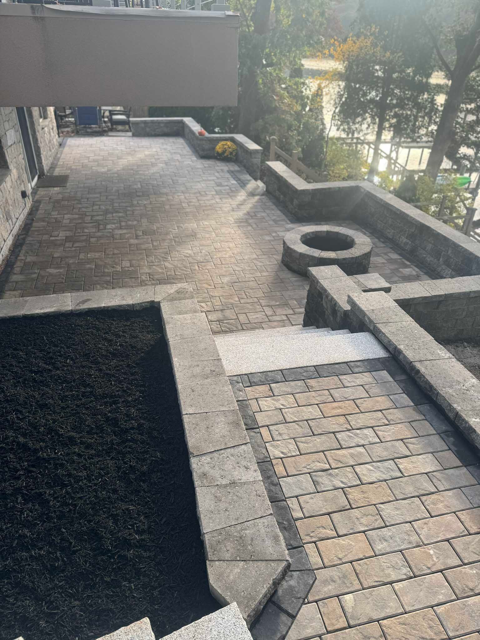 A stone patio with a built-in fire pit, stone retaining walls, and a matching walkway leading to a garden area.