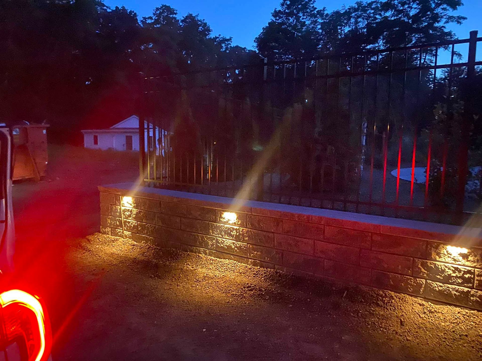 Low-angle view of a stone wall at twilight, featuring three warm LED lights illuminating the wall and surrounding ground.