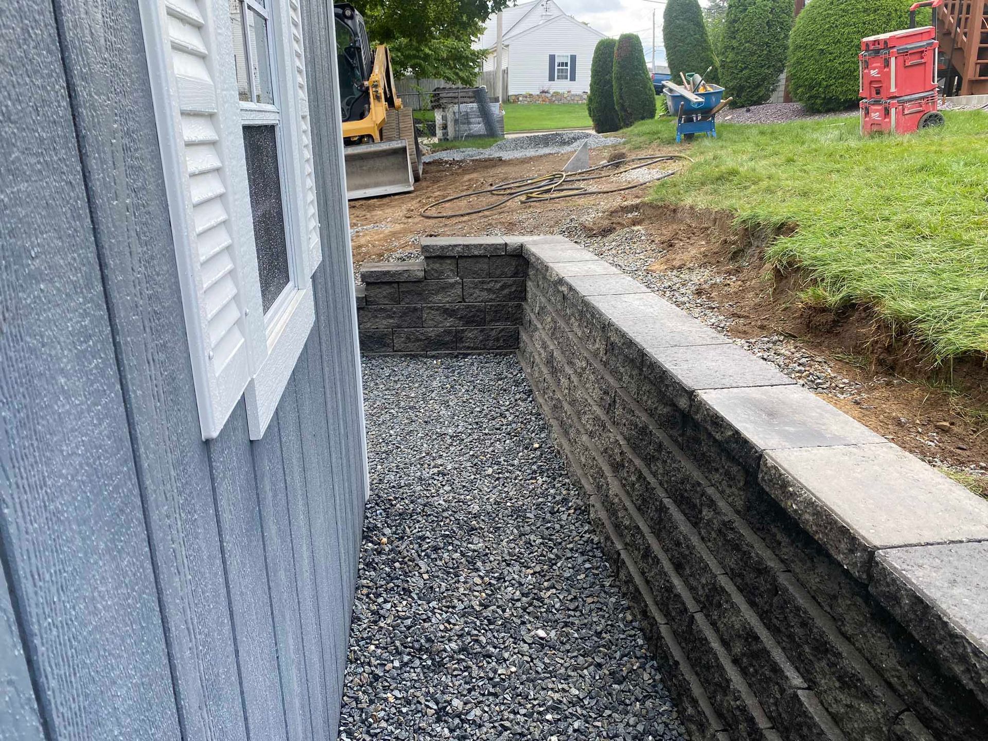 A narrow gravel path runs between the side of a blue building and a stacked stone retaining wall.