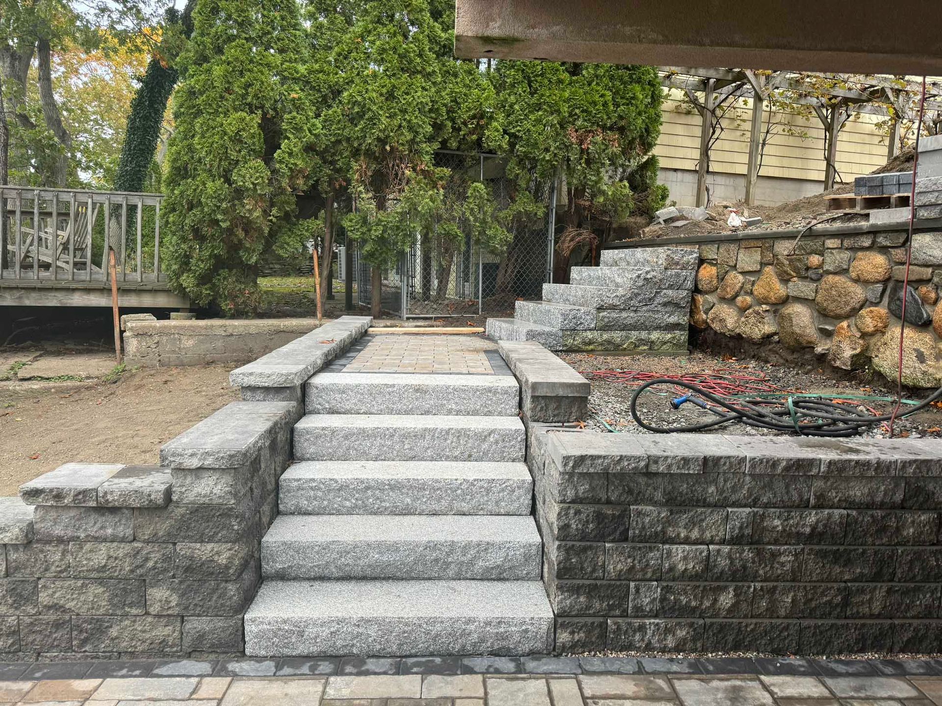 Granite steps flanked by stone retaining walls leading up to a wooden deck in a landscaped yard.