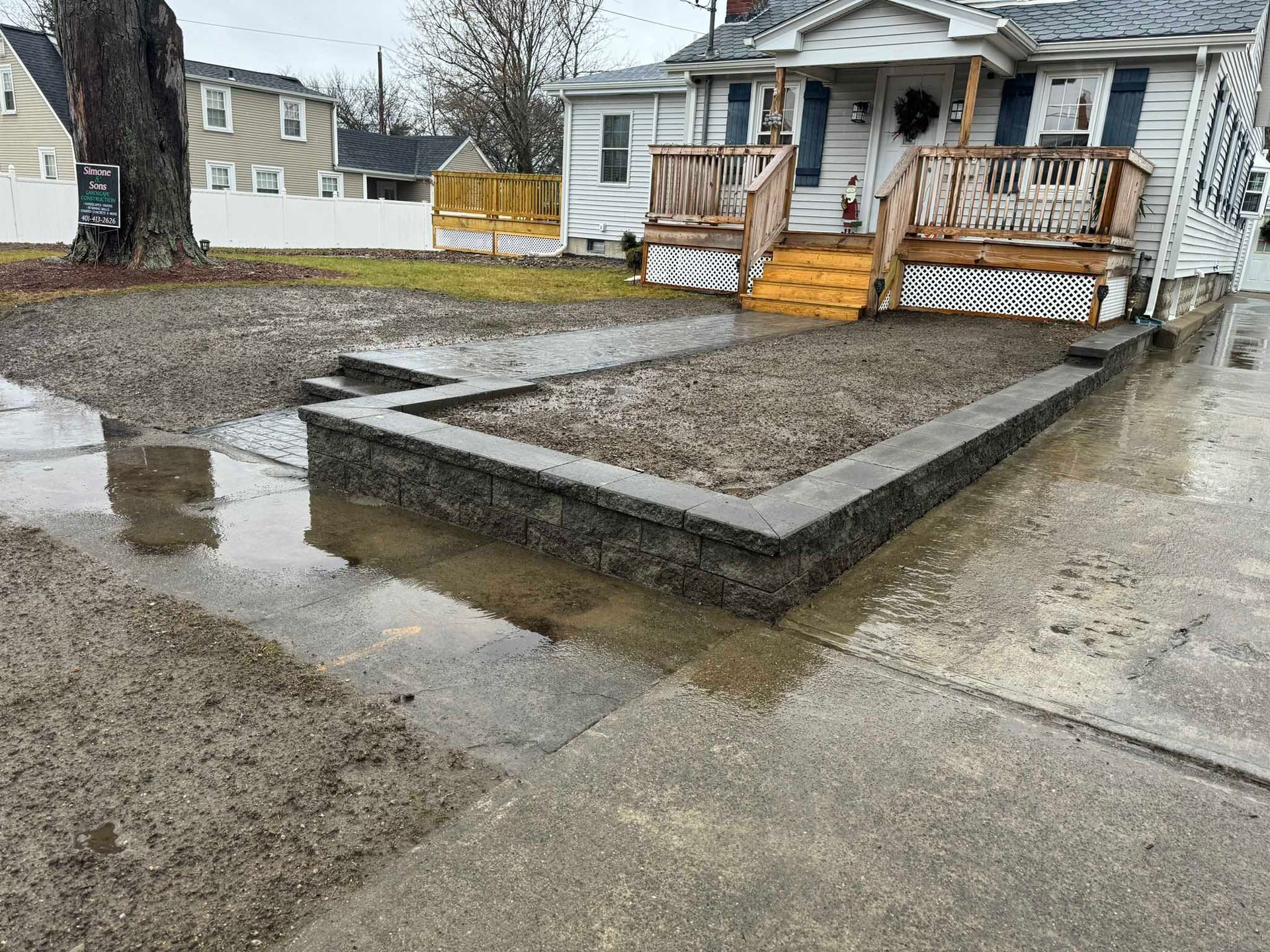 A gray retaining wall and gravel front yard area under construction in front of a house on a rainy day.