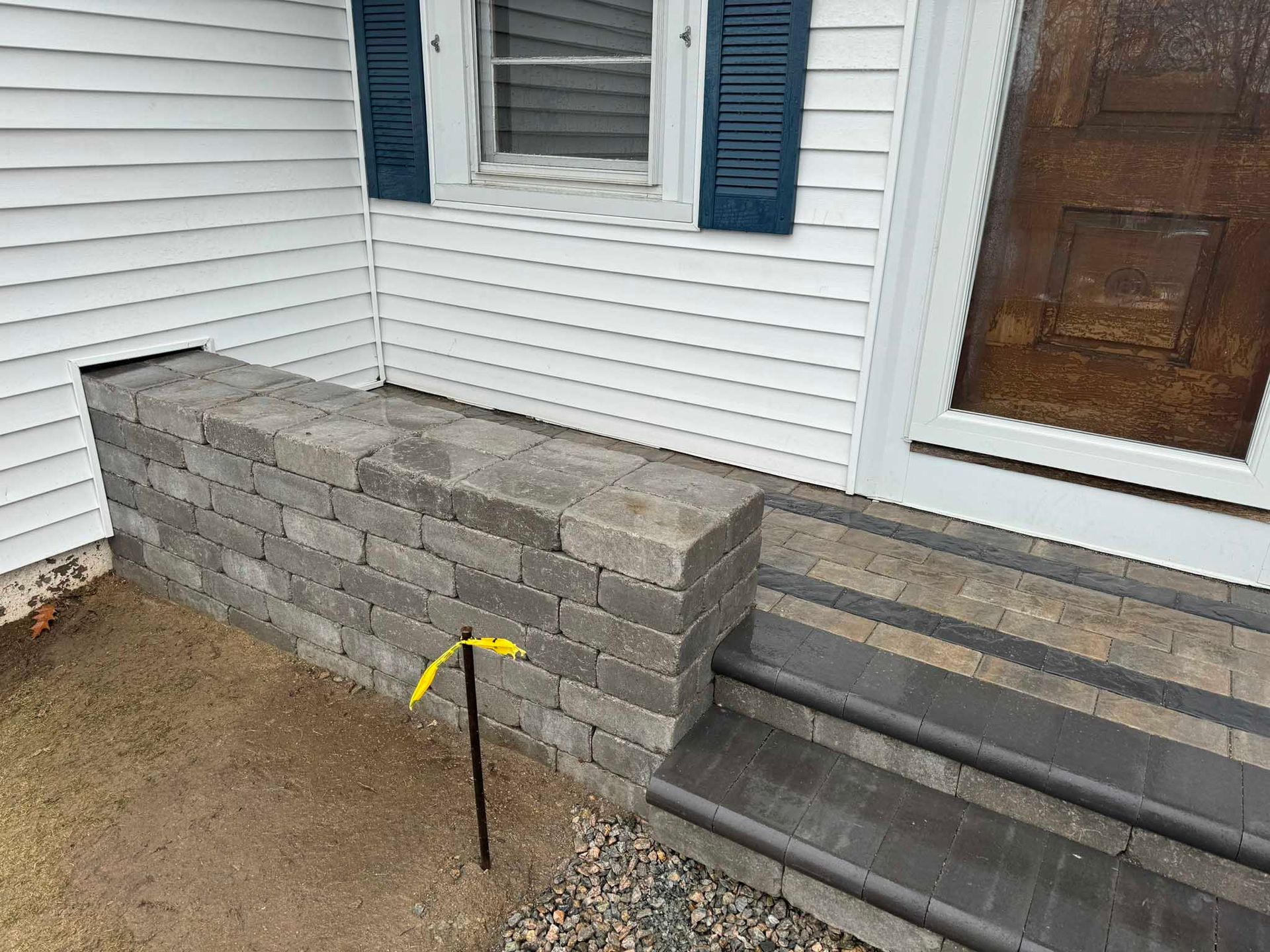 A low grey stone retaining wall built next to paved steps leading to a house entrance.