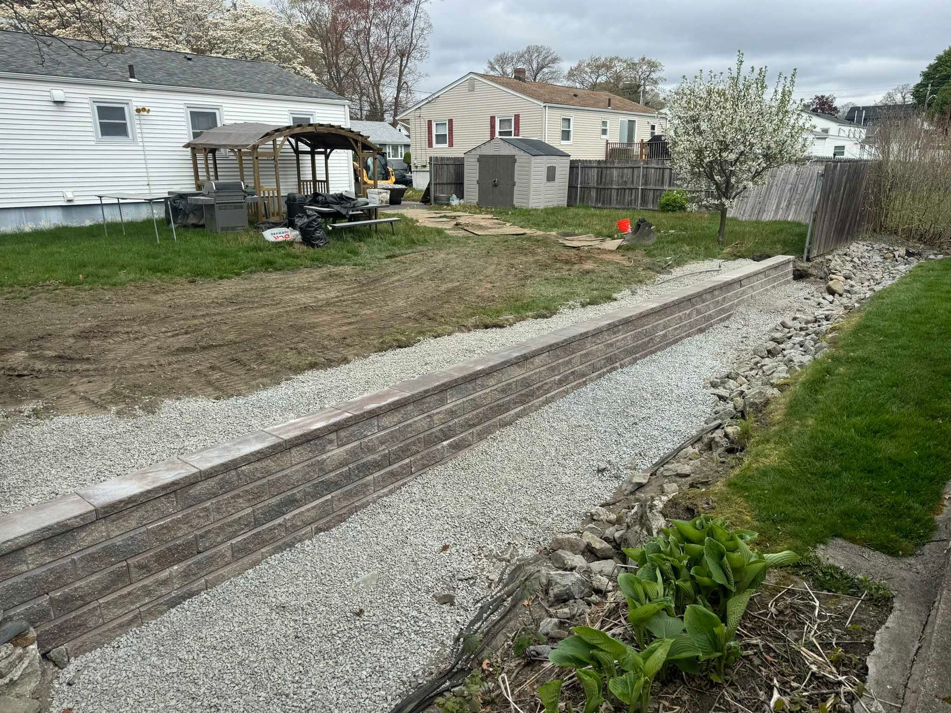 A residential backyard featuring a gravel driveway strip with wooden borders, leading toward a shed and house.