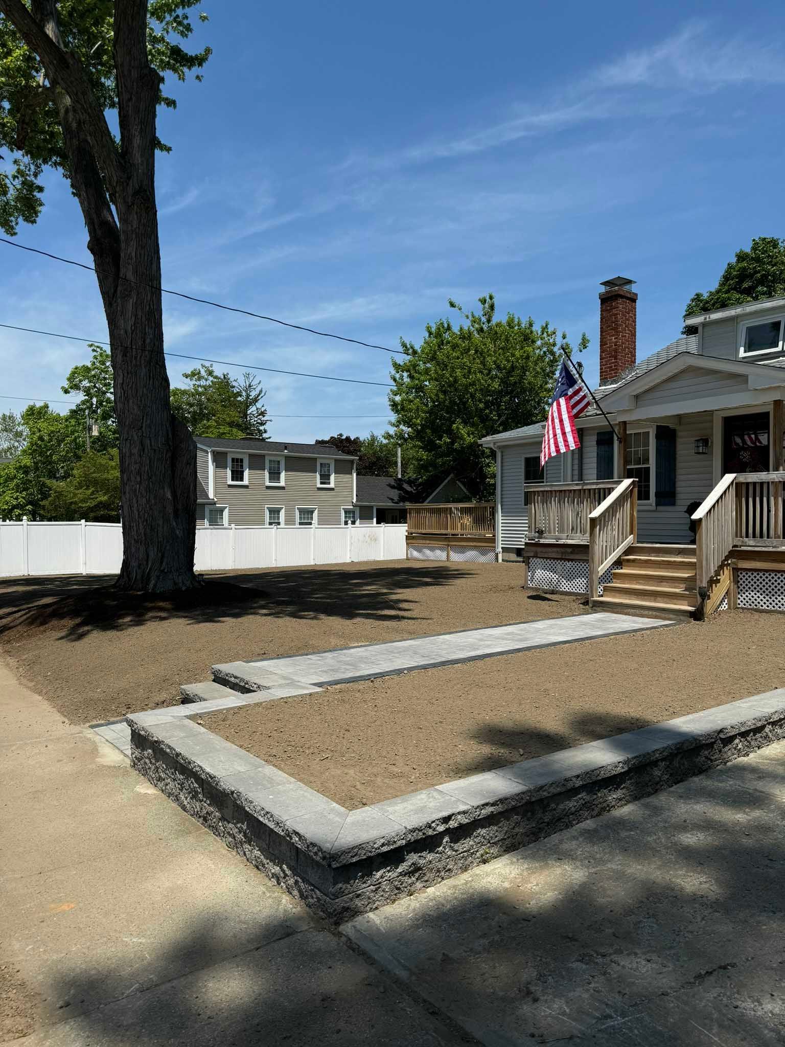 A house with a newly installed stone retaining wall and a walkway leading to the front porch under a clear blue sky.