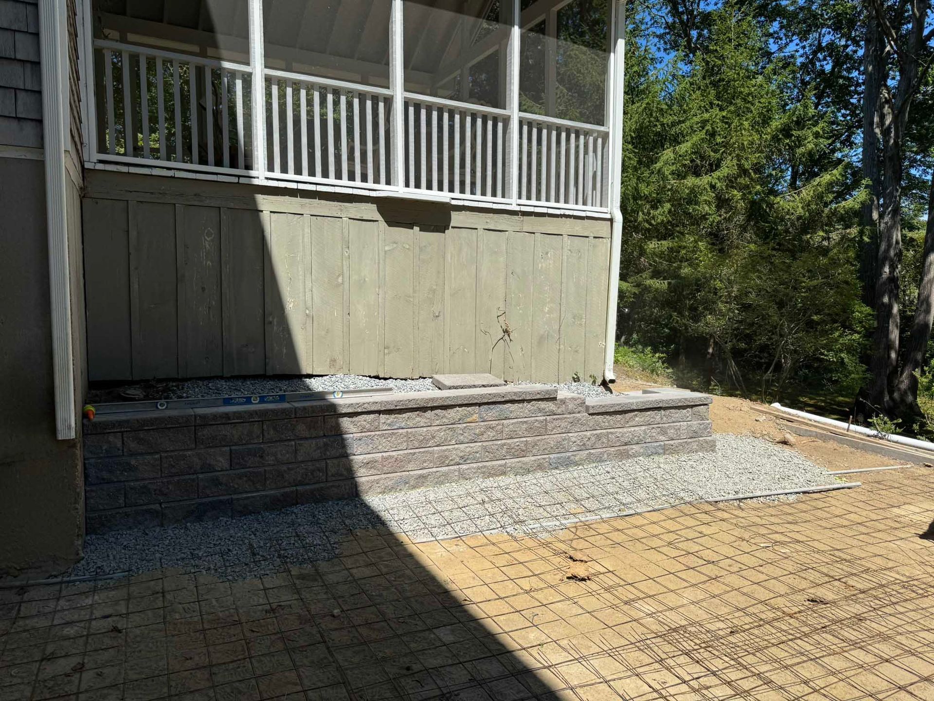 A stone retaining wall built against a house deck, with a gravel transition between the wall and a paver patio.