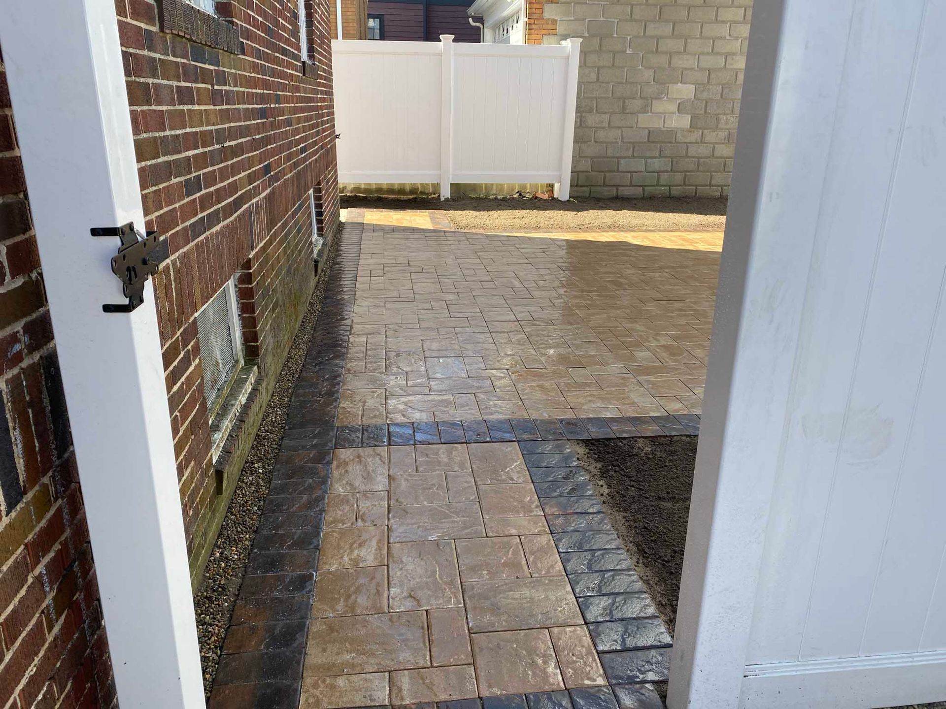 A brick building sits next to a newly paved stone patio and walkway featuring a tan center with a dark grey border.