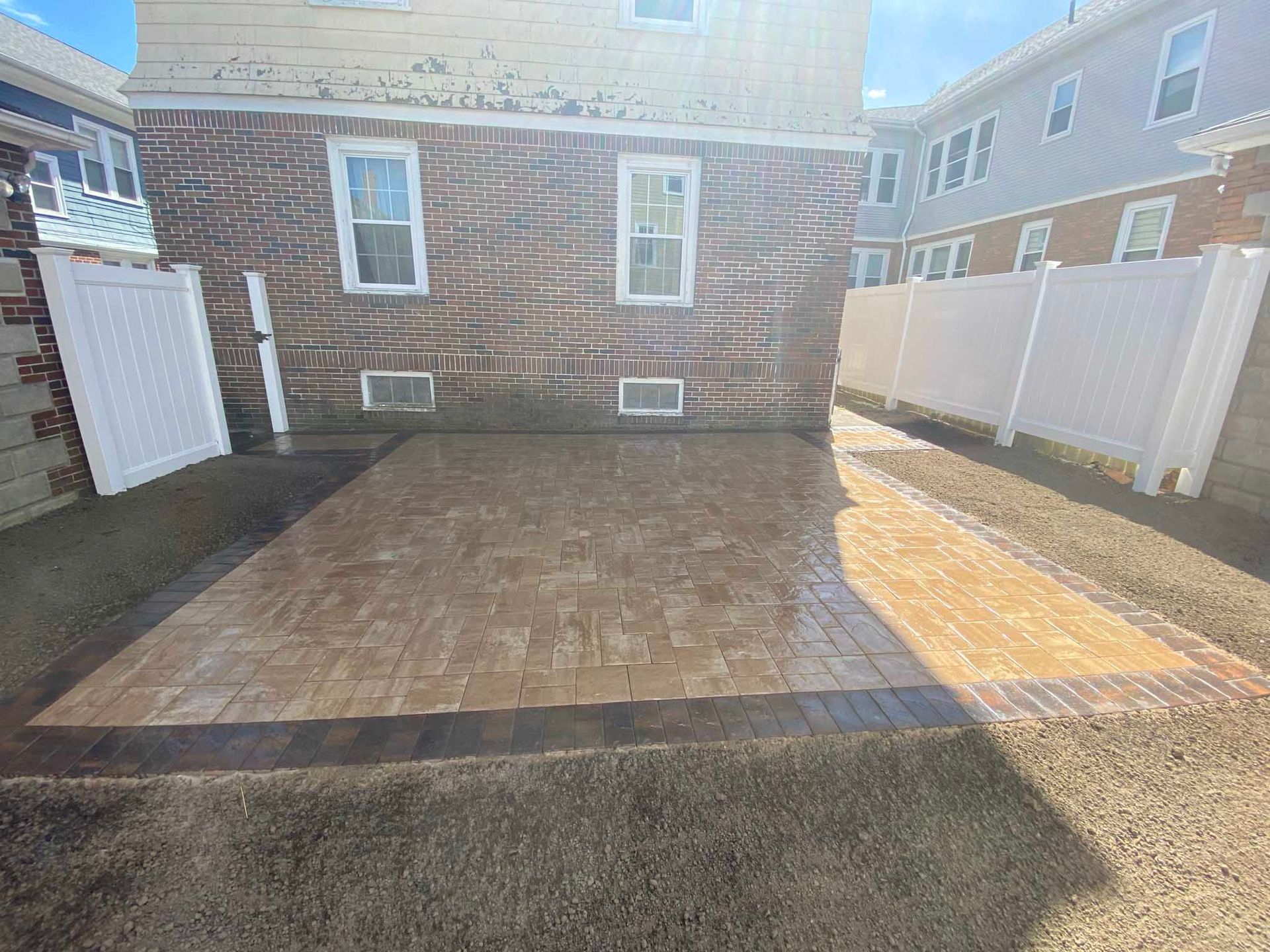 A newly installed rectangular paver patio with a dark border sits in the backyard of a residential house.