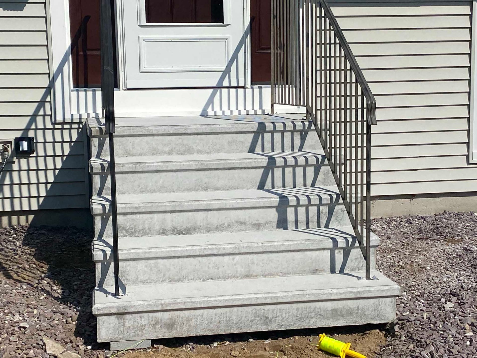 A set of five gray concrete steps leading to a white front door, flanked by dark metal railings on both sides.