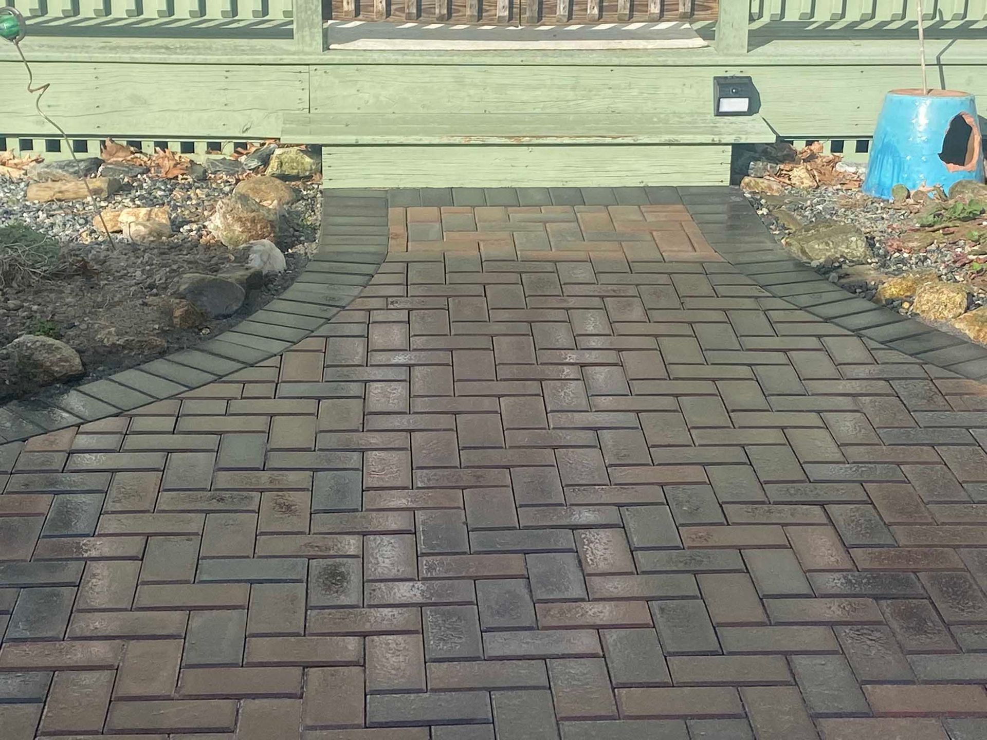 A brick pathway with a herringbone pattern leads to a light green wooden deck.