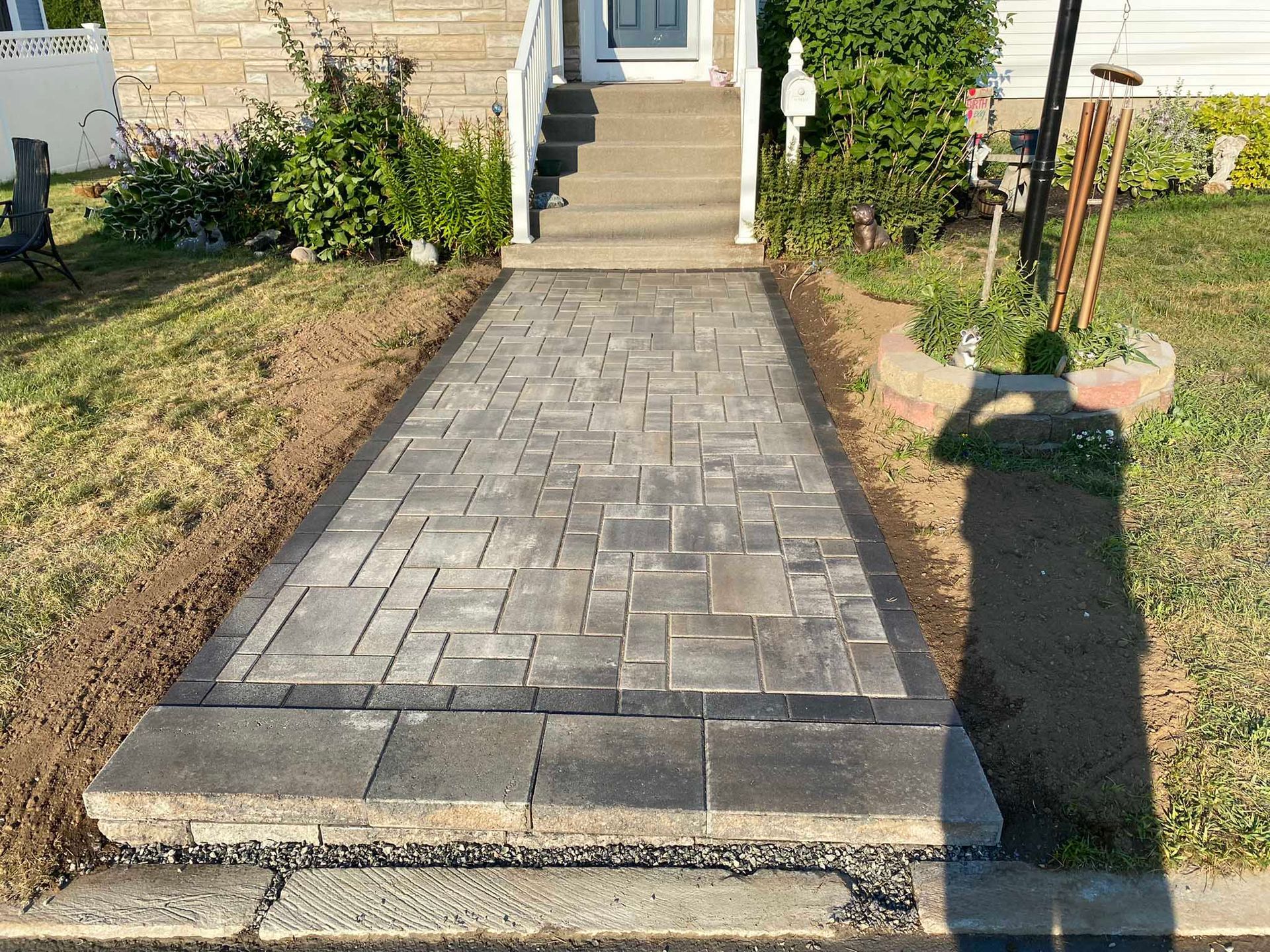 A grey paver stone walkway leads from the street to a residential front porch with stone stairs.