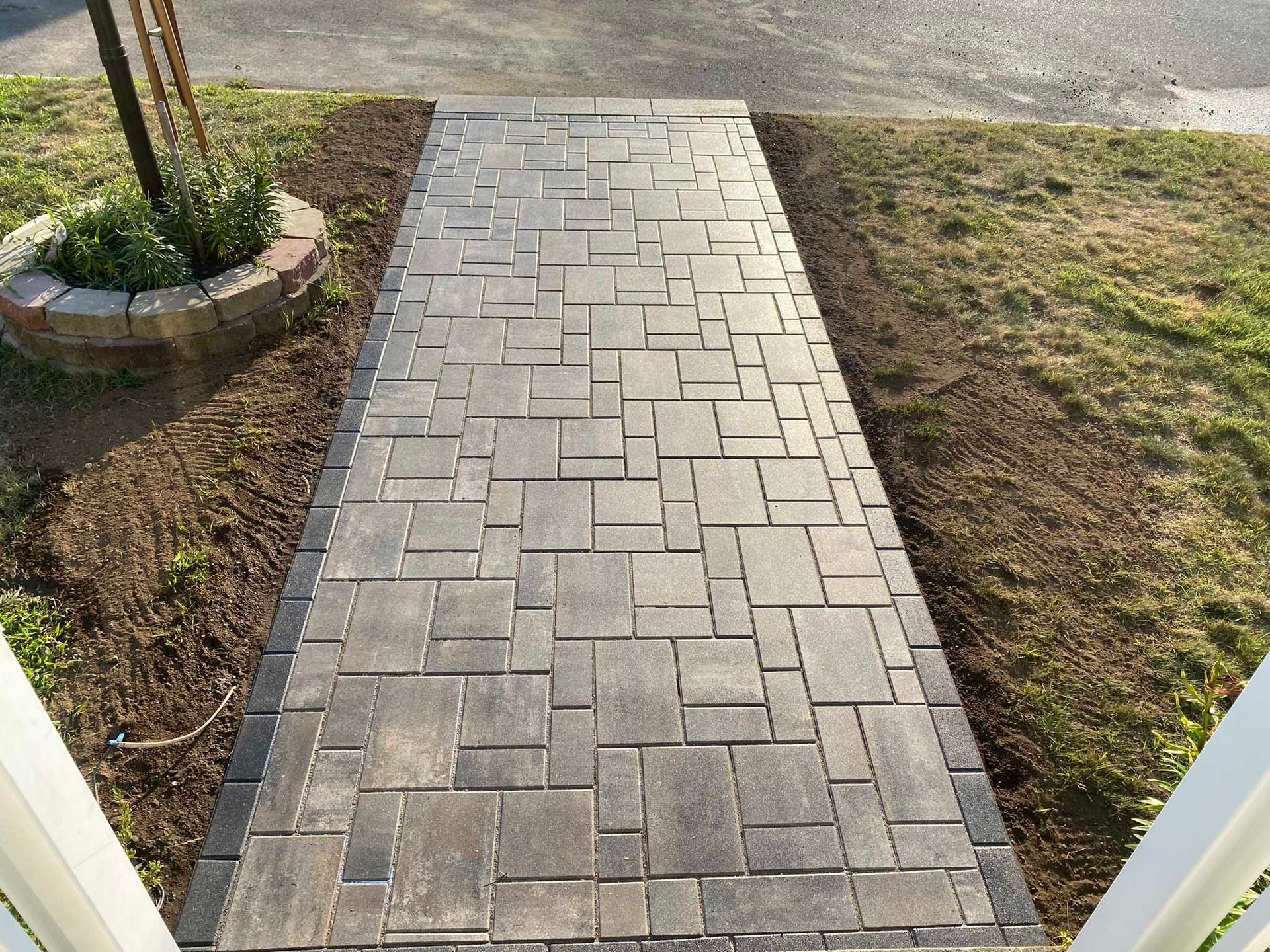 A straight walkway made of rectangular, gray-toned stone pavers with a dark border, bordered by grass and mulch.