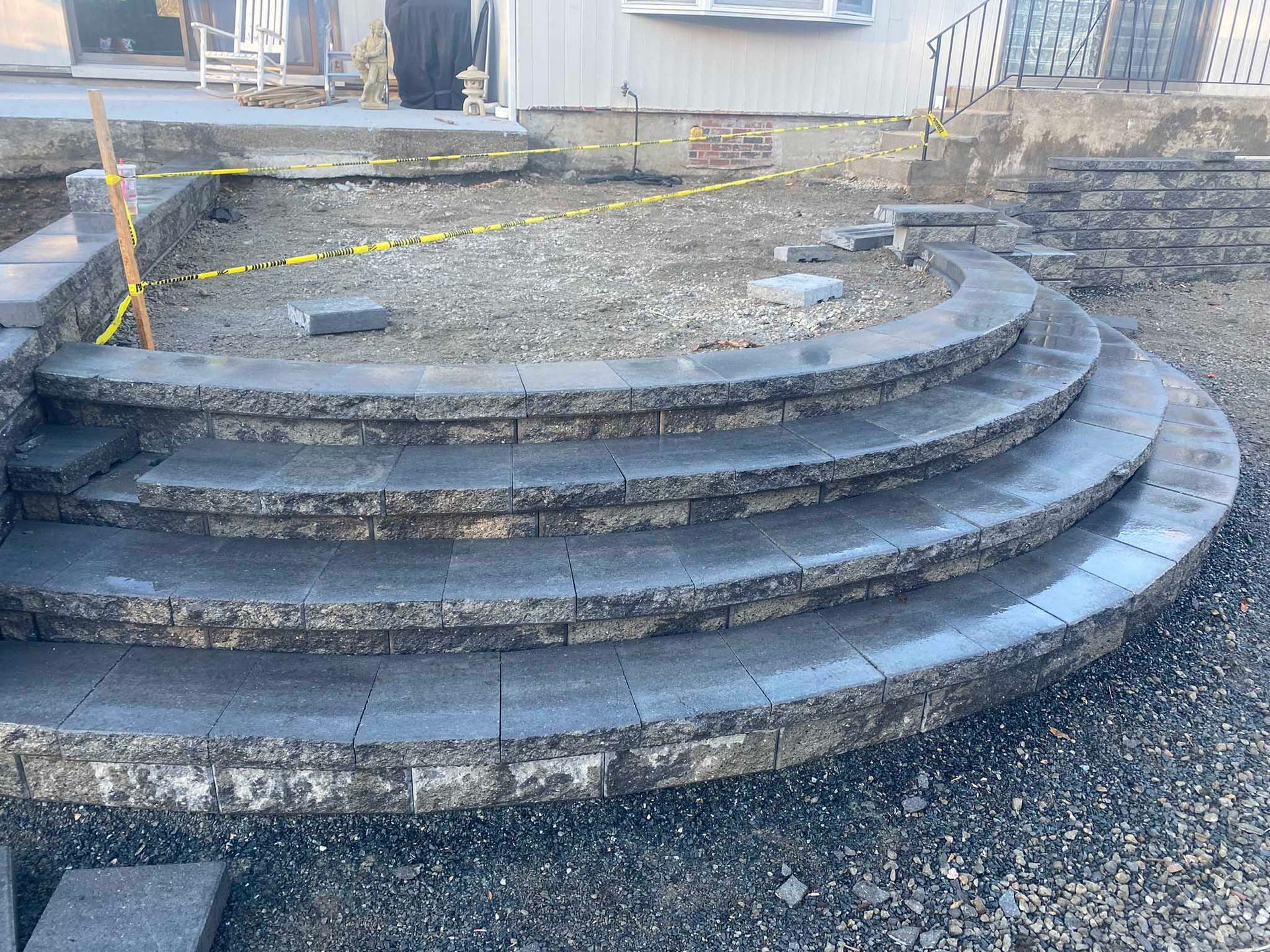A curved staircase made of grey stone pavers leading to a gravel patio area under construction.