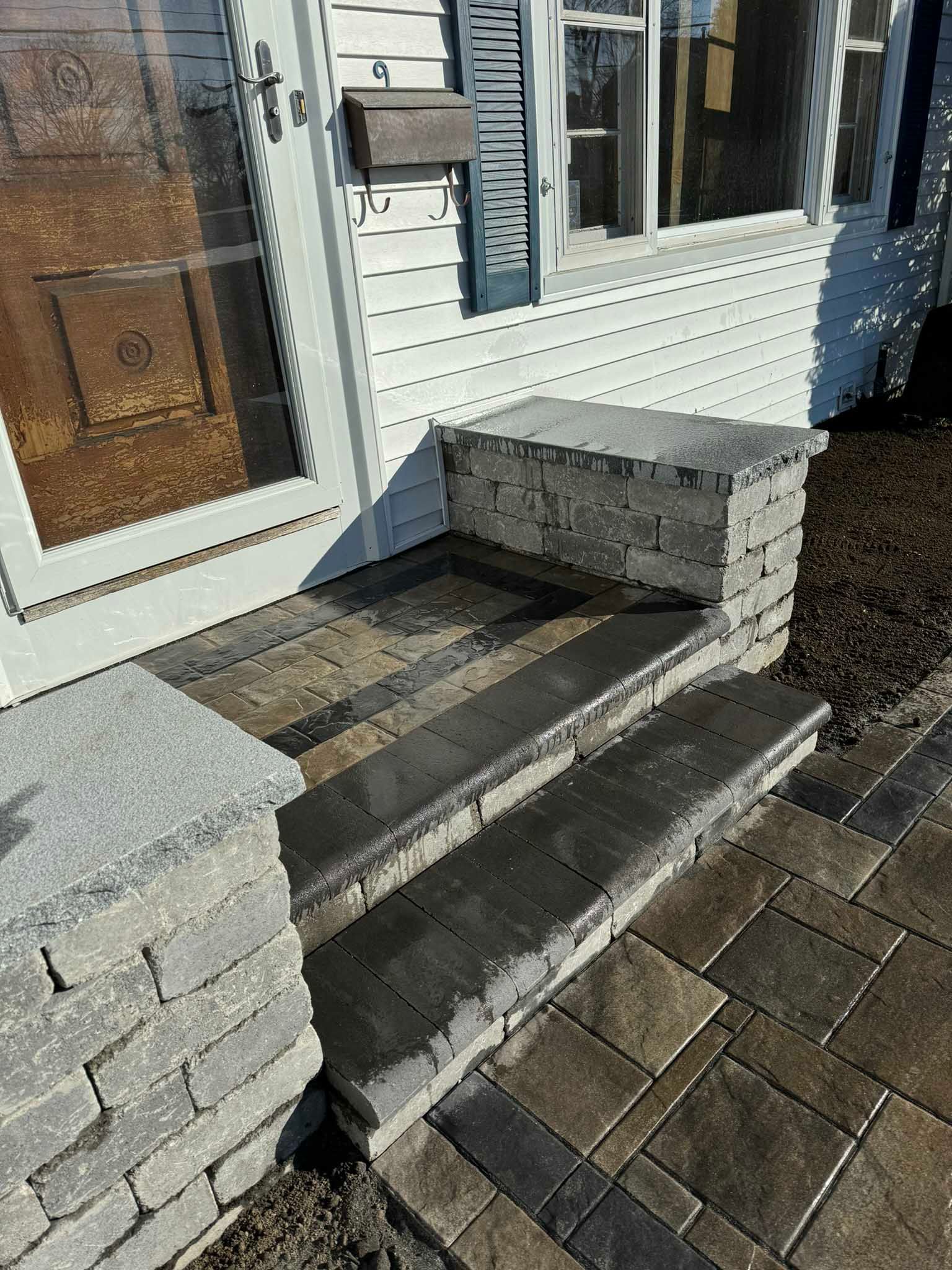A stone entryway with two wide steps leading up to a house door, framed by low stone walls with flat granite caps.