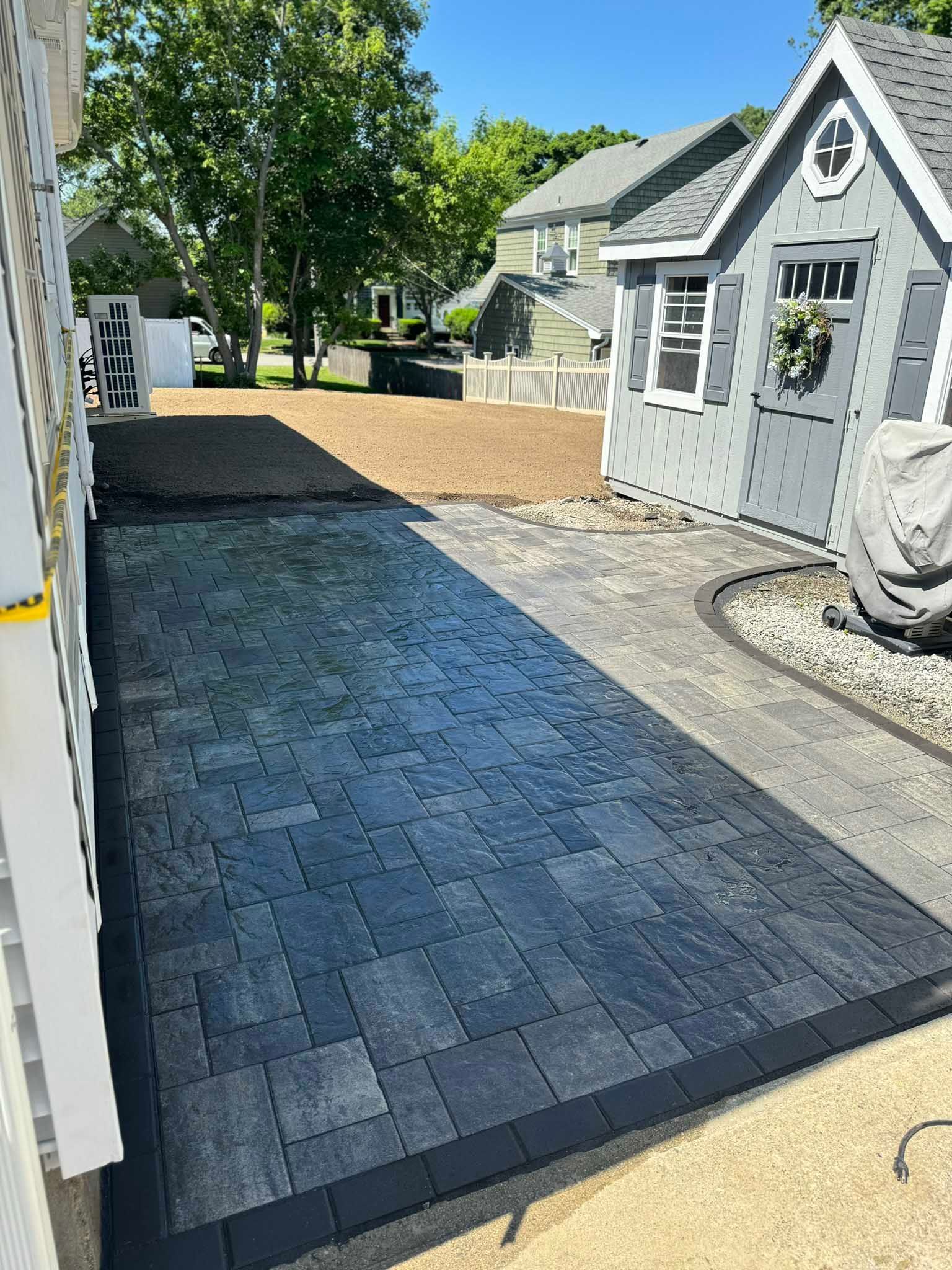 A newly installed rectangular stone paver patio next to a gray shed in a residential backyard.