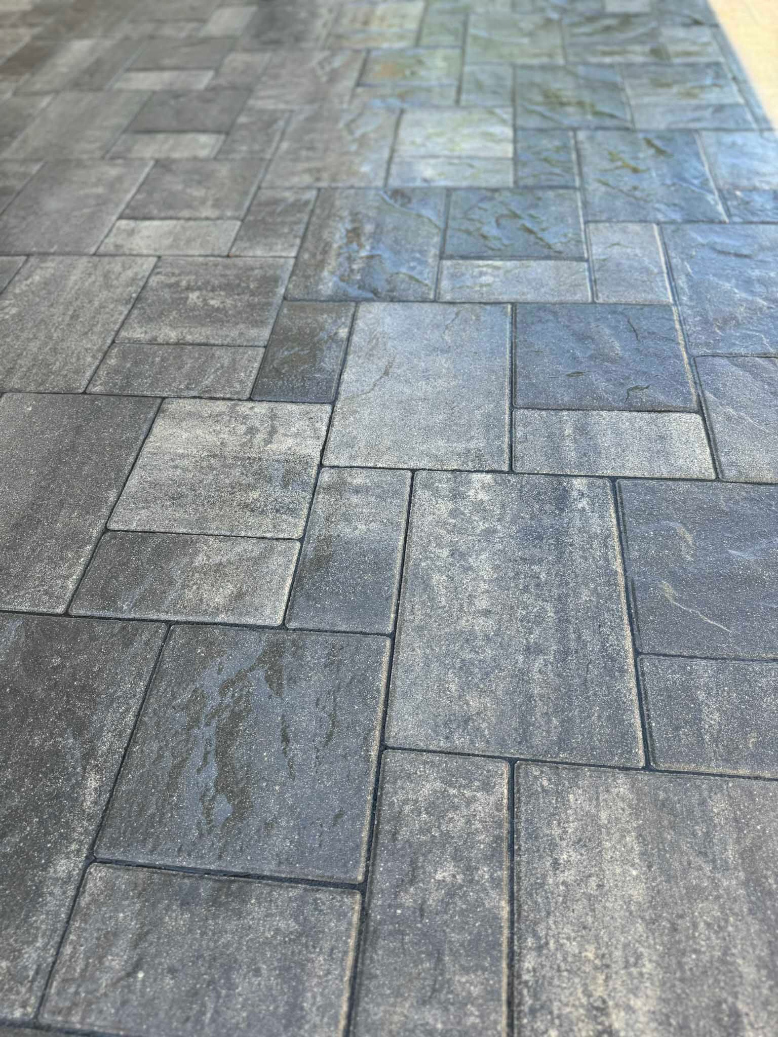 A close-up of a patio surface featuring interlocking gray and charcoal stone pavers in a rectangular pattern.