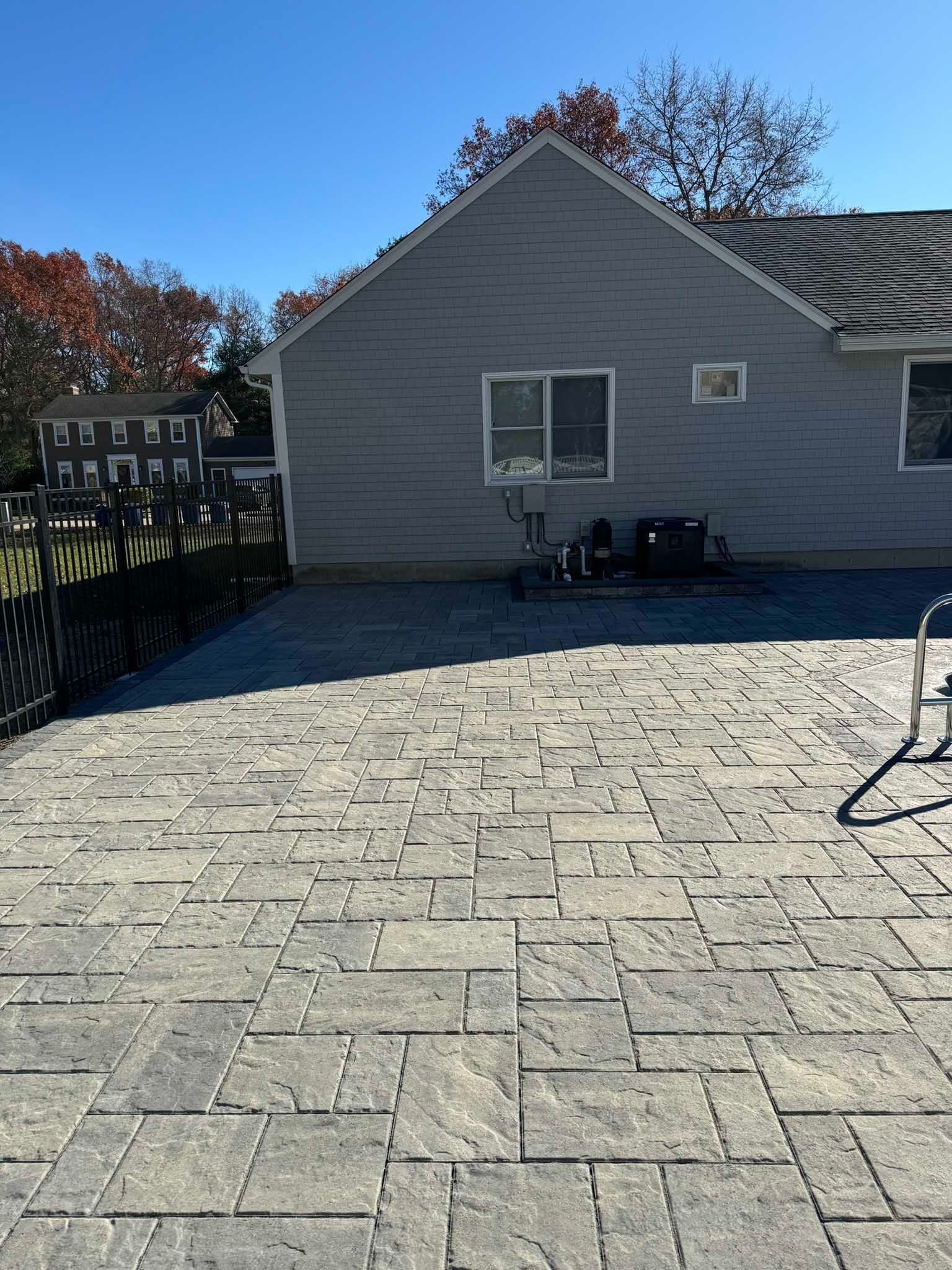 A gray house exterior with a large, newly installed gray stone paver patio on a sunny day.