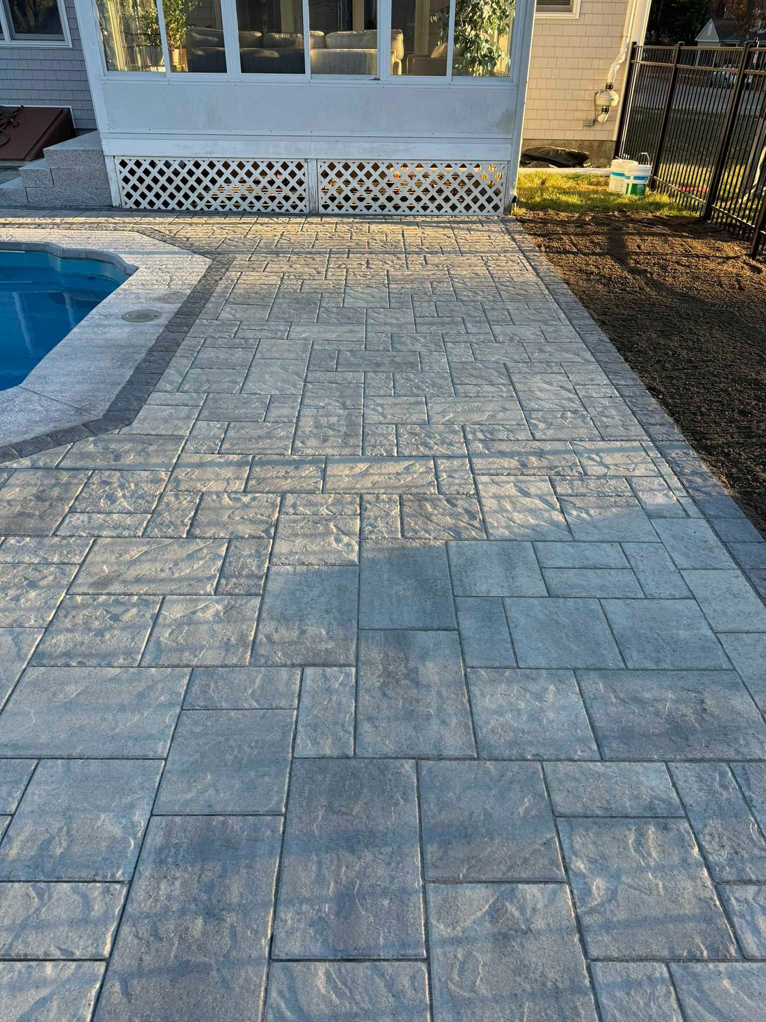 Grey concrete patio pavers arranged in a repeating pattern next to a swimming pool and a white screened-in patio.