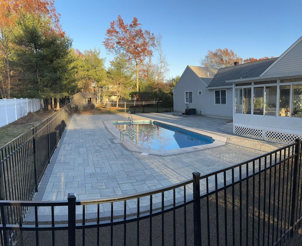 Backyard swimming pool with winter cover, black fence, and house beside autumn trees