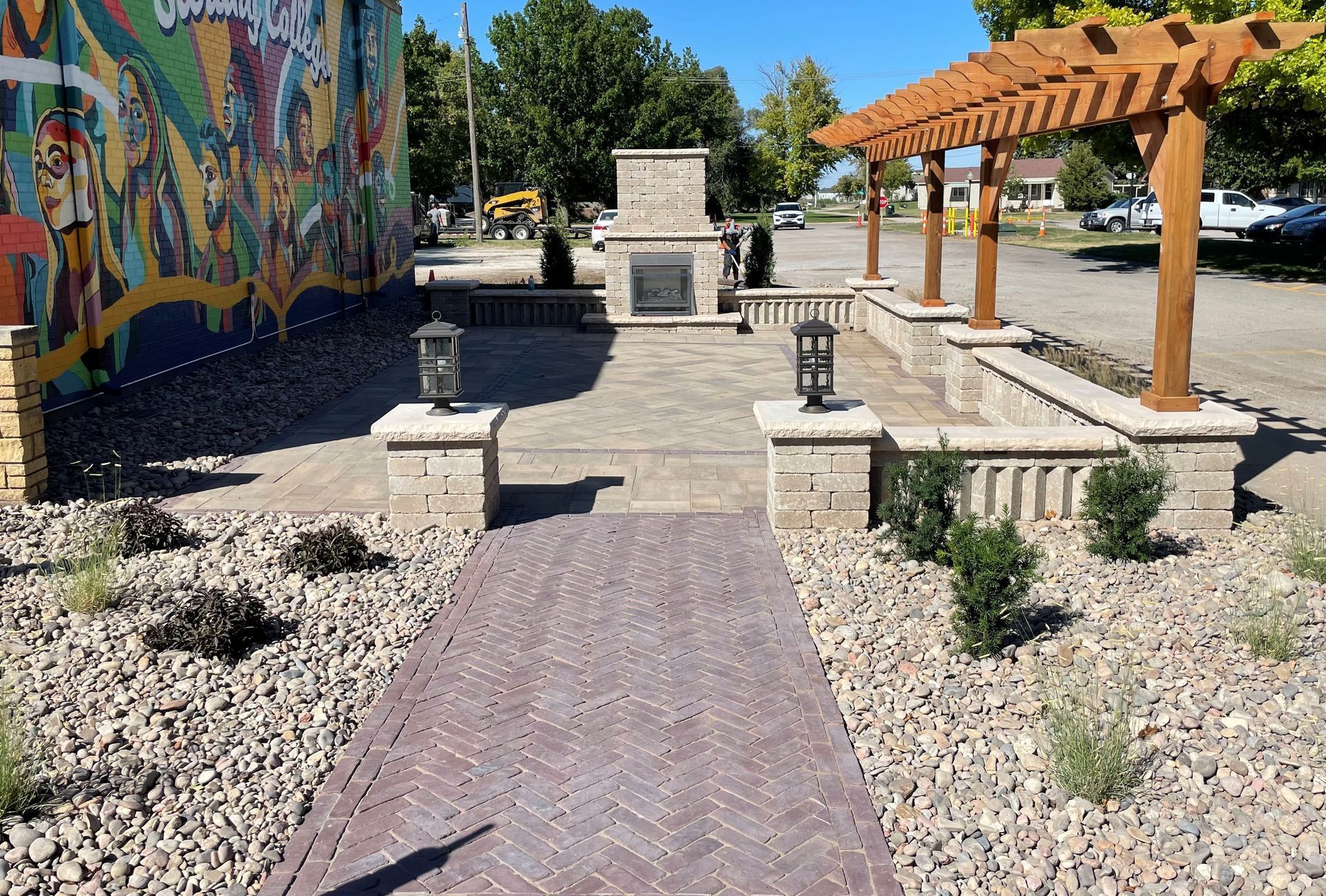Brick patio with pergola, fireplace, and landscaping next to a building with a mural.
