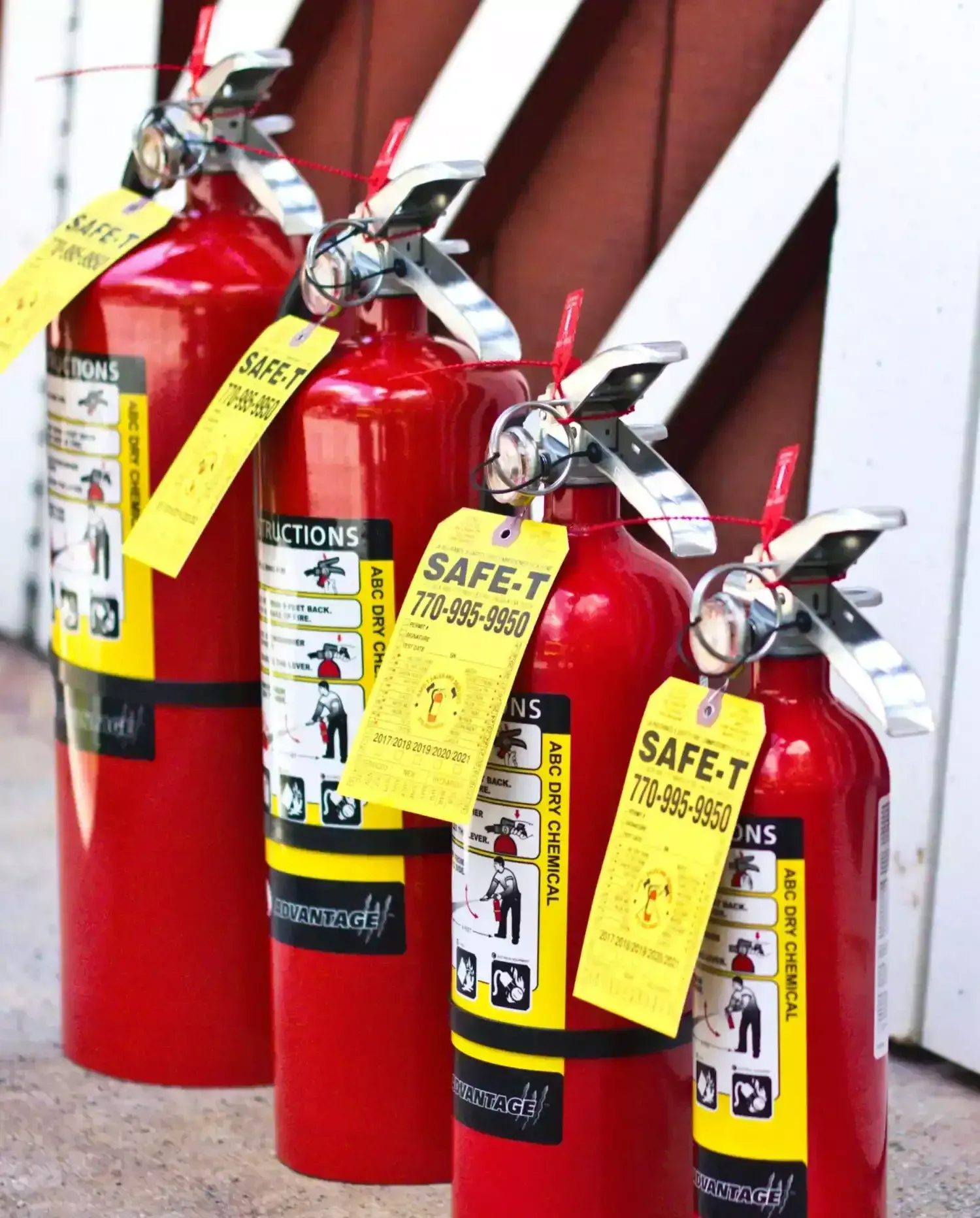 Red fire extinguisher mounted on a gray exterior wall beside a sliding glass door and wooden deck.