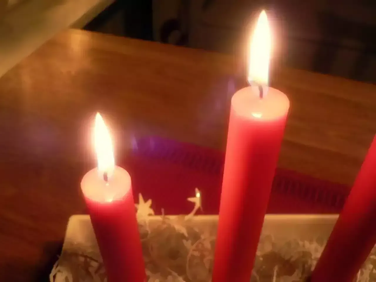 Three lit red candles in a dim room on a wooden table
