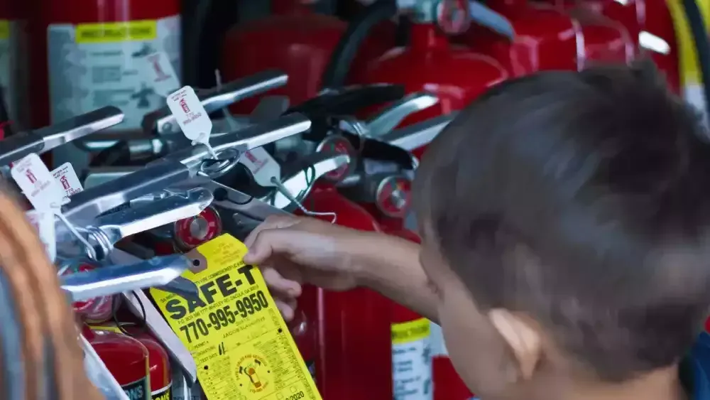 Child reaching toward toy drones on a store shelf with a yellow sale tag and red fire extinguishers behind them
