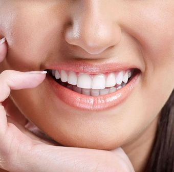 Close-up of a smiling mouth showing white teeth while a finger points to the teeth