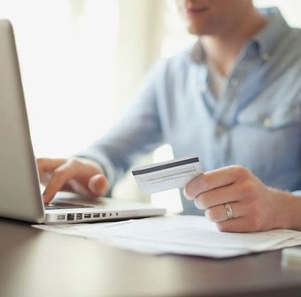 Person using a laptop and holding a credit card at a desk