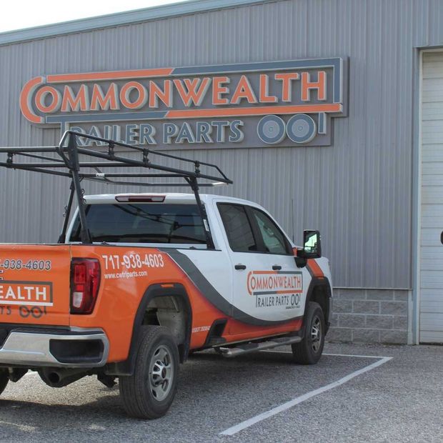 A white and orange service truck parked in front of a building branded "Commonwealth Trailer Parts."
