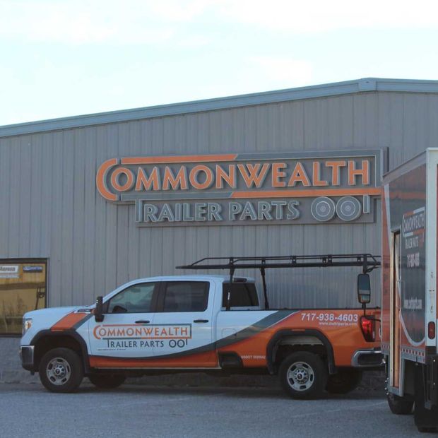A white pickup truck with orange branding parked in front of a building labeled Commonwealth Trailer Parts.