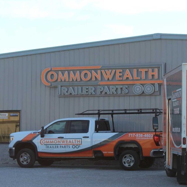 A white pickup truck with orange branding parked in front of a building labeled Commonwealth Trailer Parts.