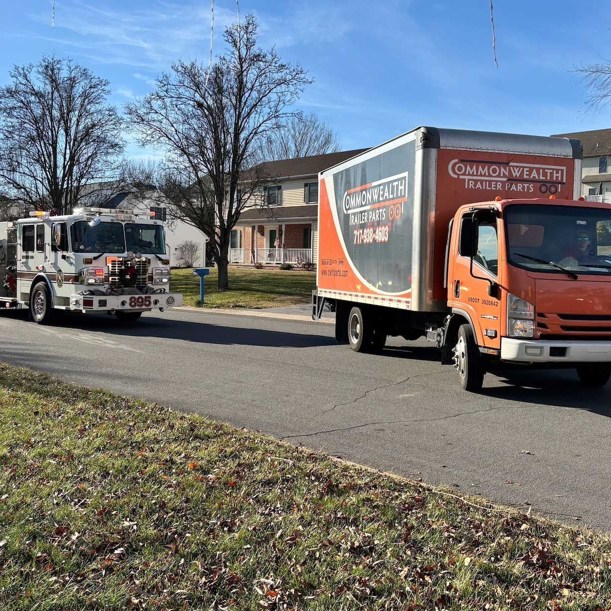 A fire truck and an orange Commonwealth Trailer rental box truck driving on a suburban street on a sunny day.