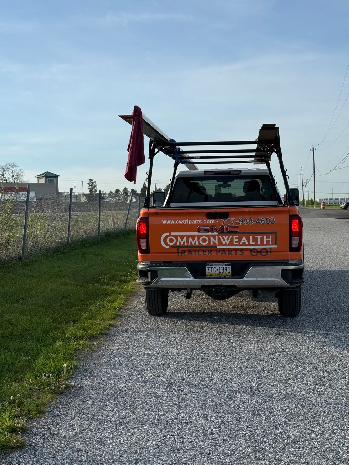 Utility truck on a gravel road beside a fenced field, carrying ladders and tools.