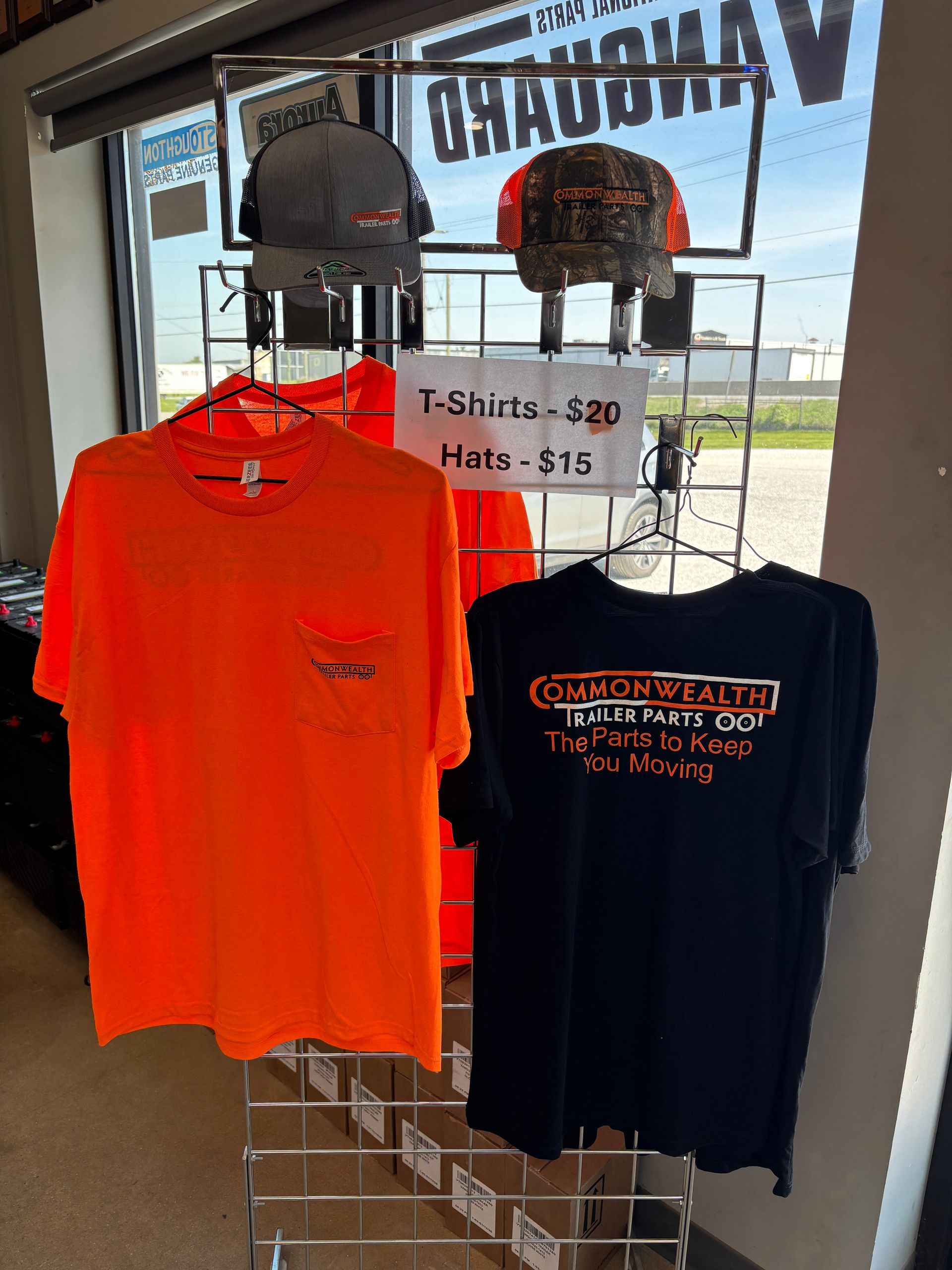 T-shirts on display in a shop window, including bright orange and black shirts with price signs.