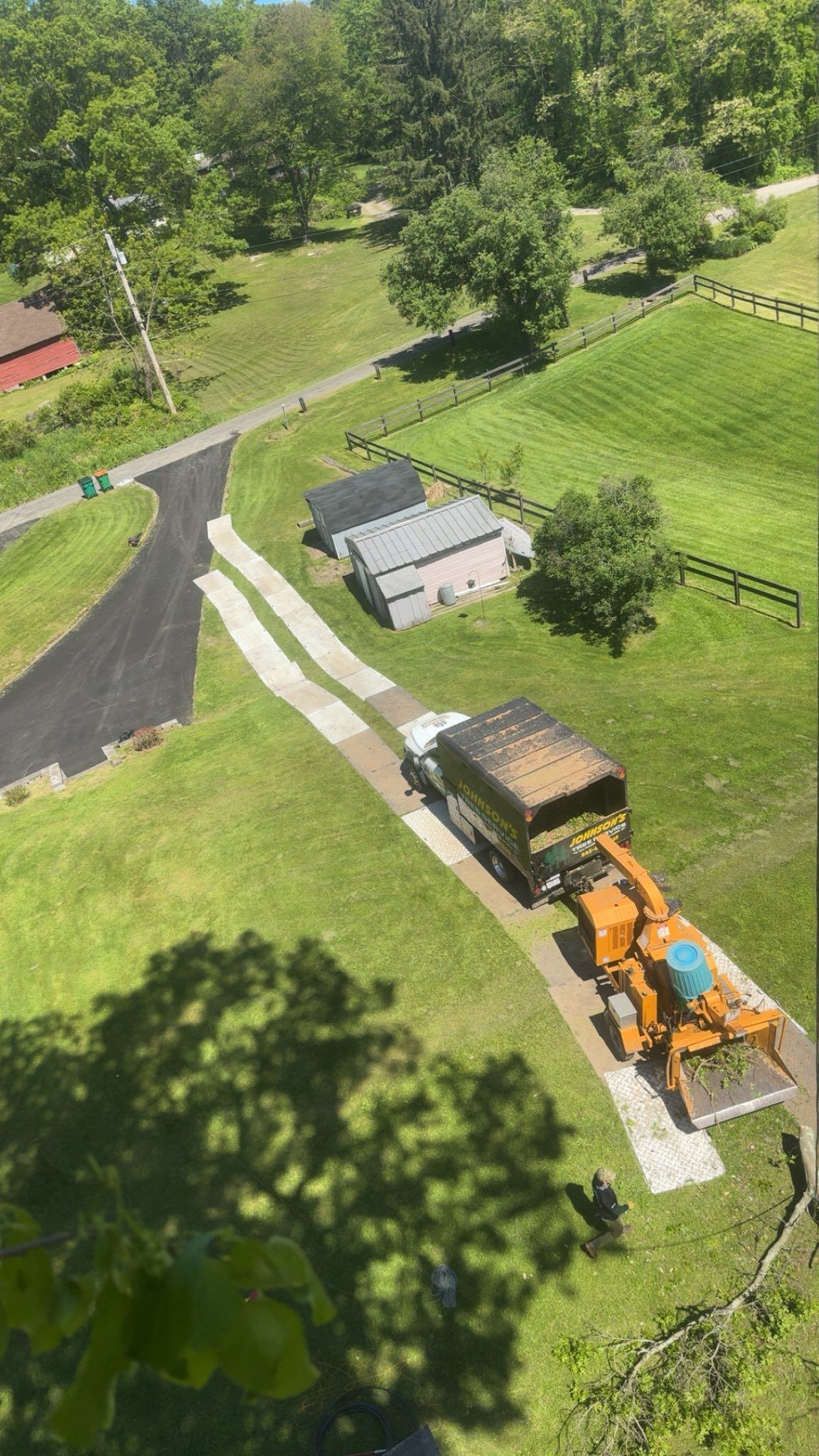 Aerial view of a lawn tractor hauling a cart along a paved path beside a small shed and green fields.