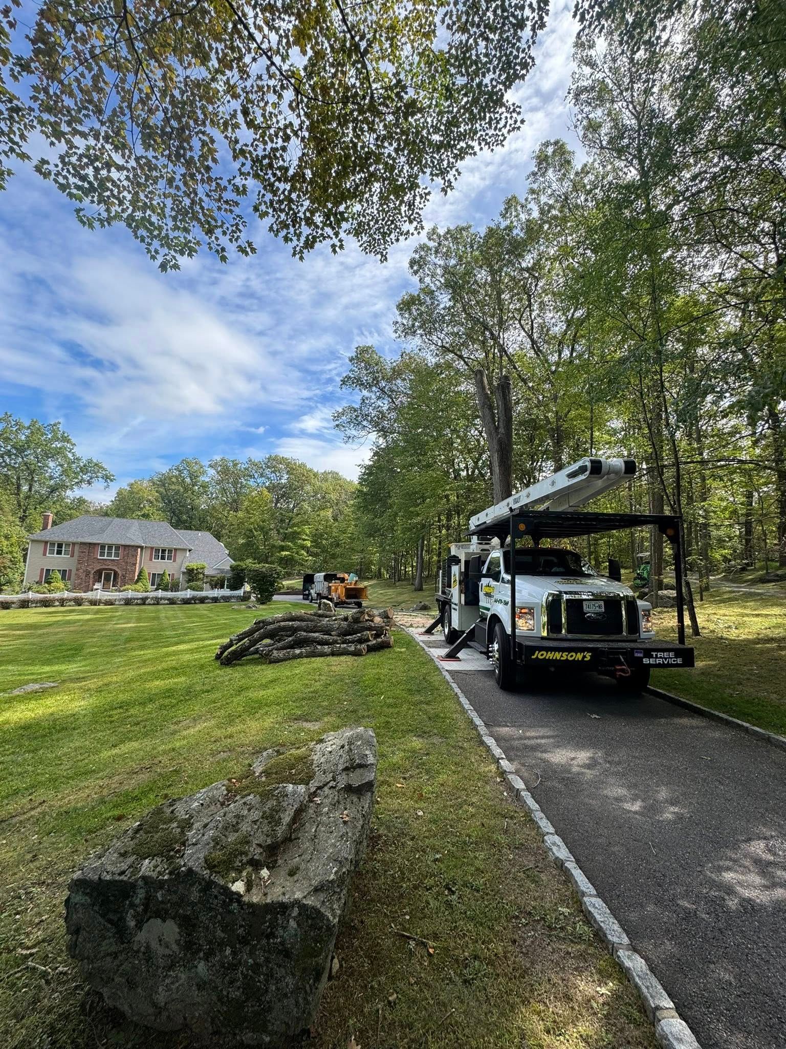 Work crew and utility truck on a gravel path beside a grassy yard and house, under trees and blue sky