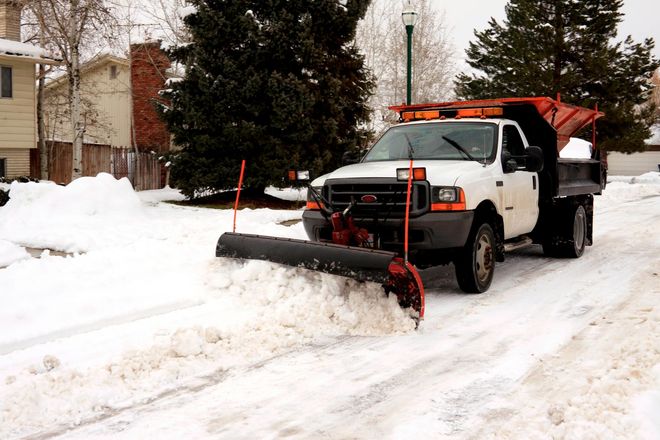 White pickup truck with snowplow clearing a snowy residential street after a snowfall