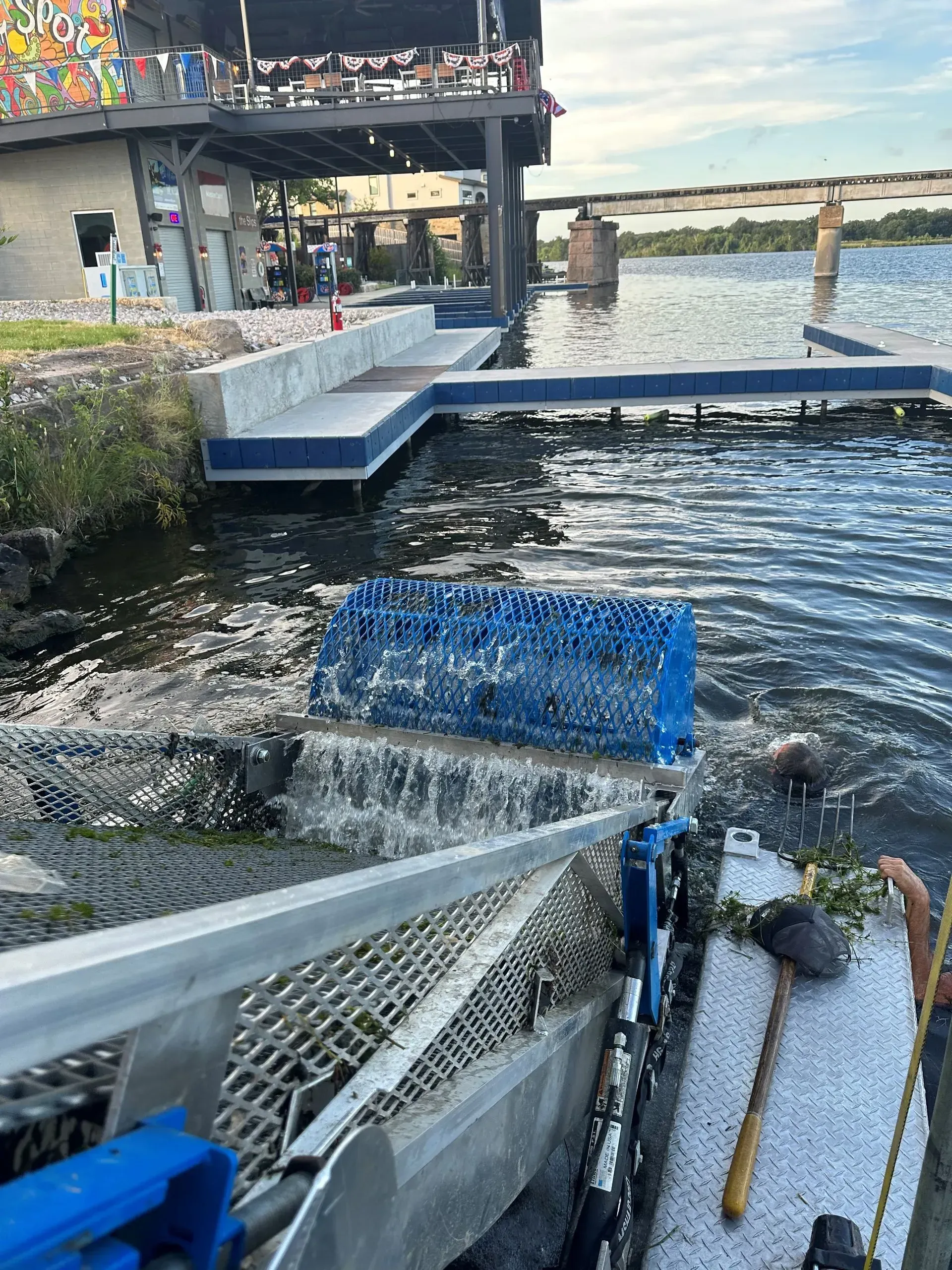 A machine cleaning debris from a body of water near a dock and building.
