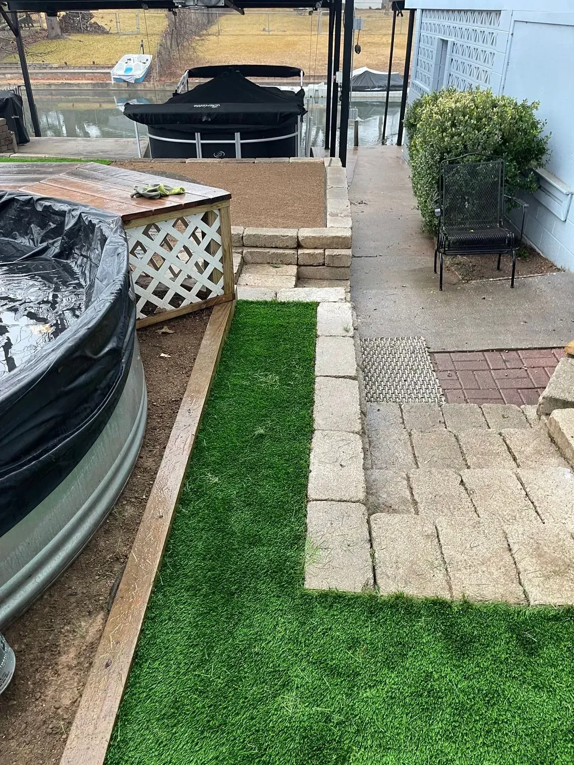A pathway of pavers and grass leads beside a hot tub with a view of a deck and water.