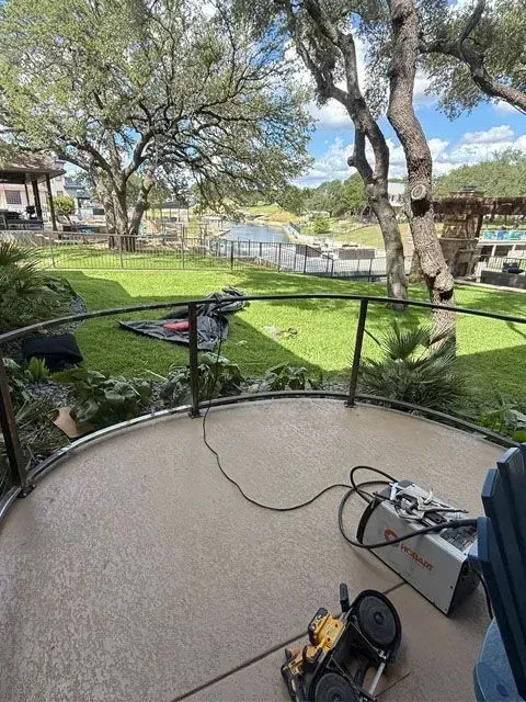 Outdoor patio with curved metal railing. Green lawn, trees, and water in the background. Tools on patio.