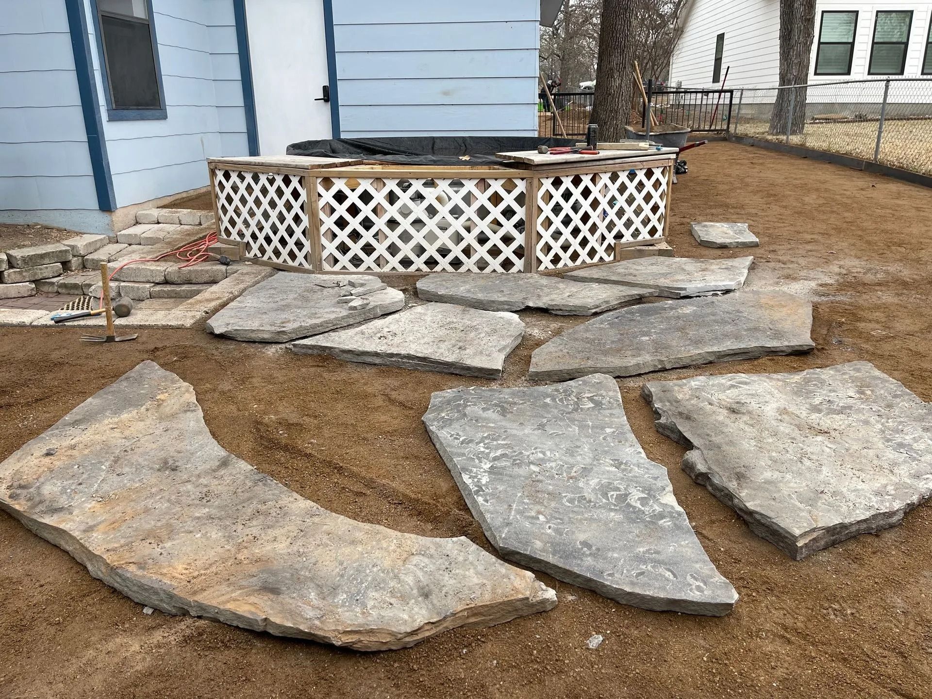 Flagstone pavers laid on dirt next to a white lattice-fenced deck.