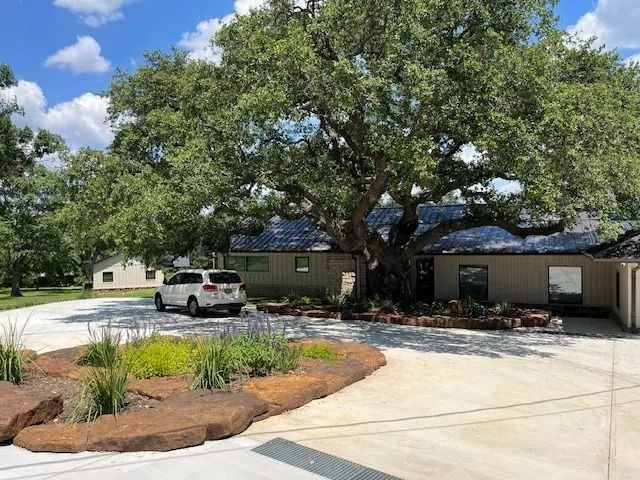 SUV parked in front of a house, shaded by a large tree, with a landscaped area in the foreground.